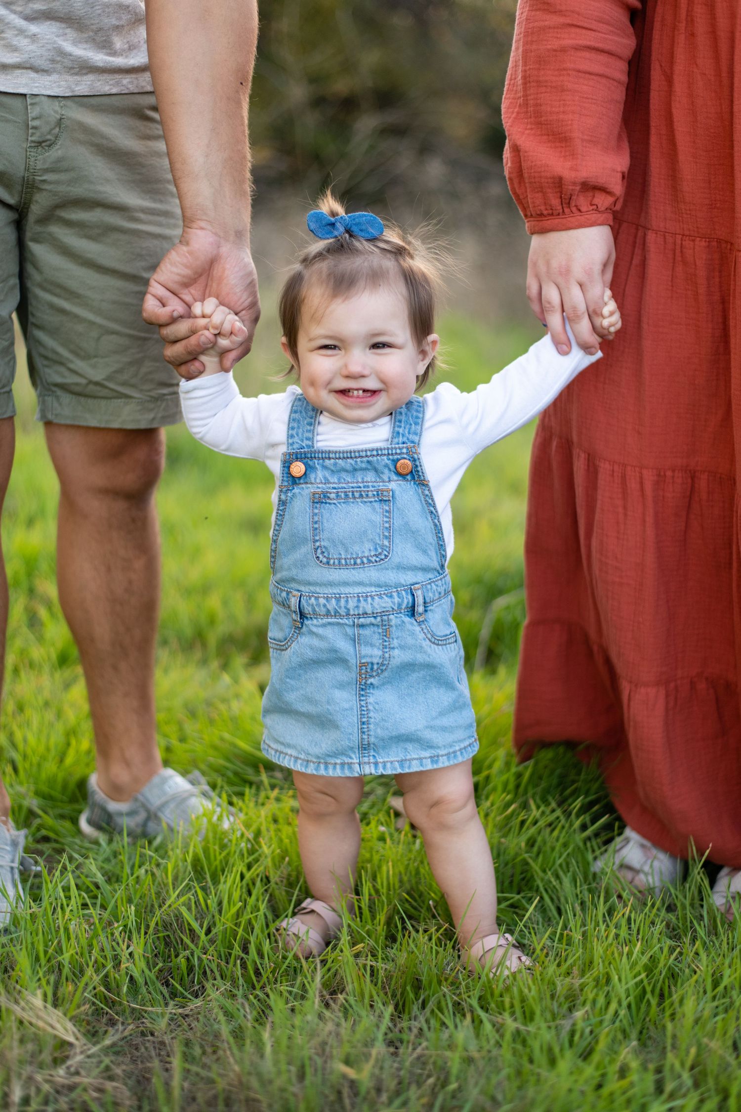 Close-up of tiny feet in denim overalls standing in green grass during family photo session.
