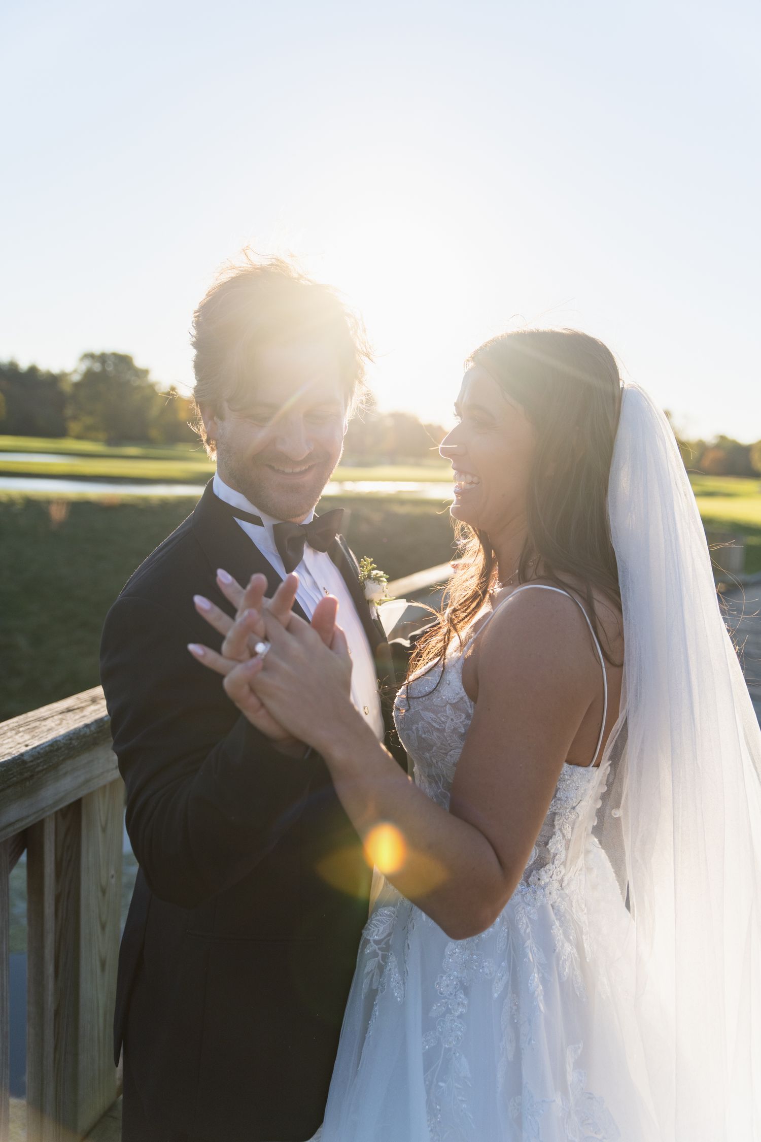 A bride and groom share a joyful moment together on a wooden deck during golden hour sunset.