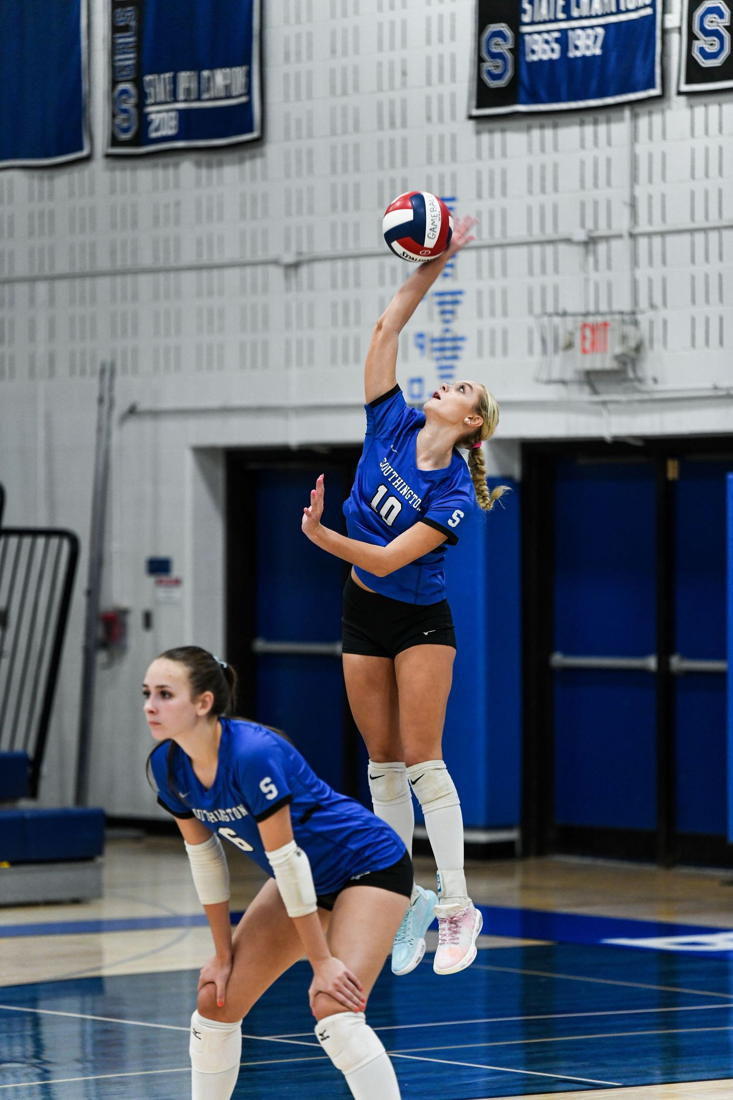 Female volleyball player in blue uniform #10 jumping to spike ball during indoor high school match.