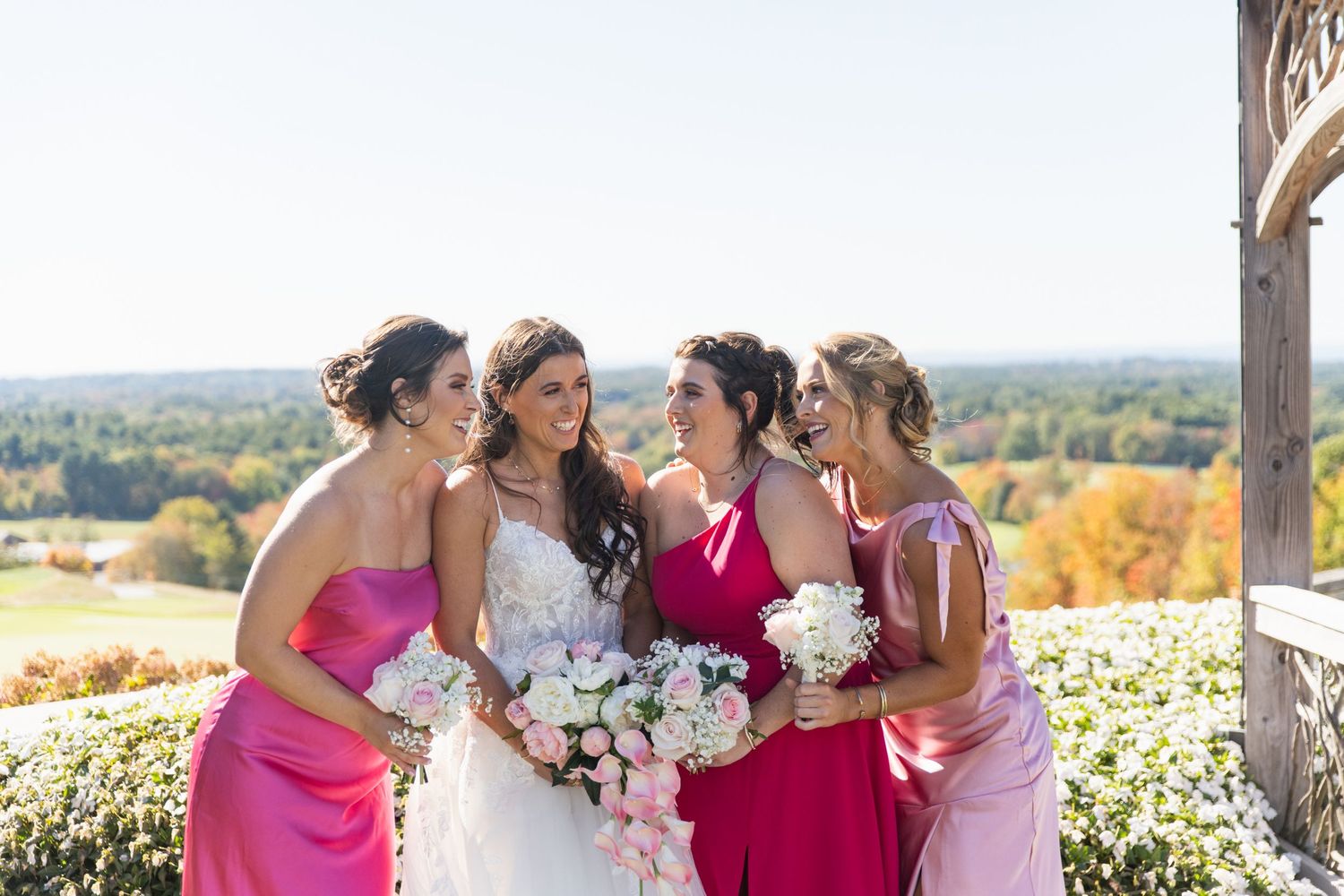 Bridesmaids in bright pink dresses gather with the bride at a scenic outdoor venue during autumn.
