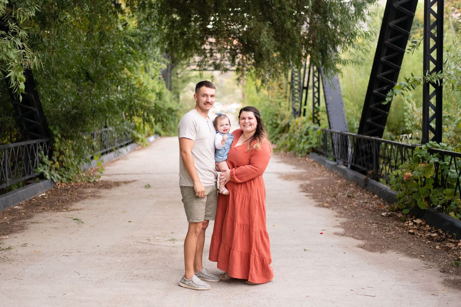 Family poses together on a tree-lined bridge pathway.