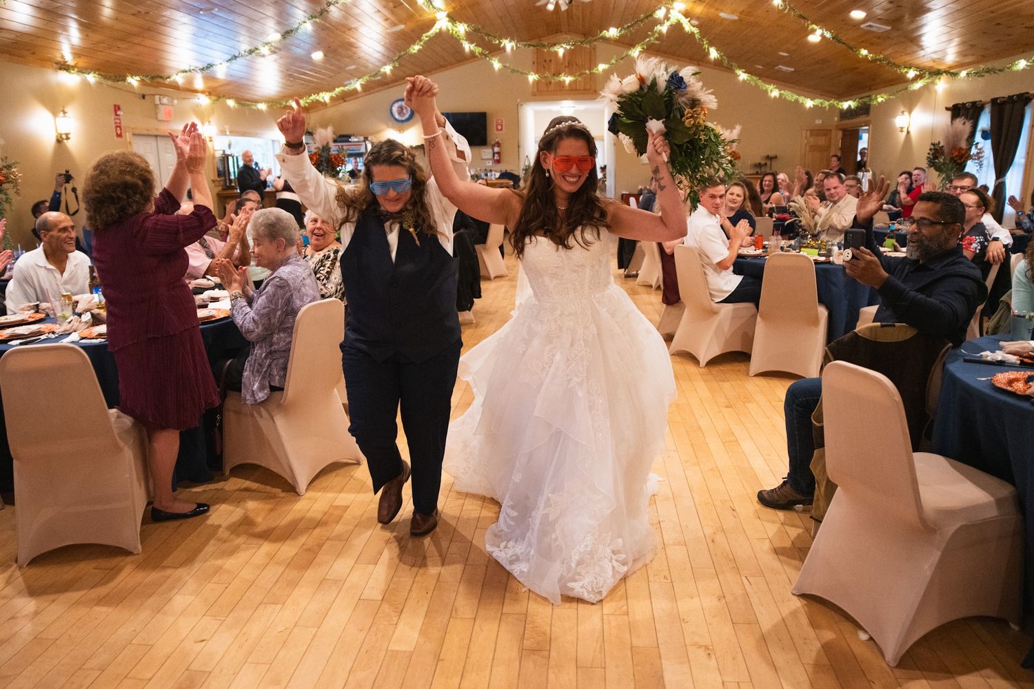 Joyful wedding celebration with guests dancing in a reception hall under string lights.