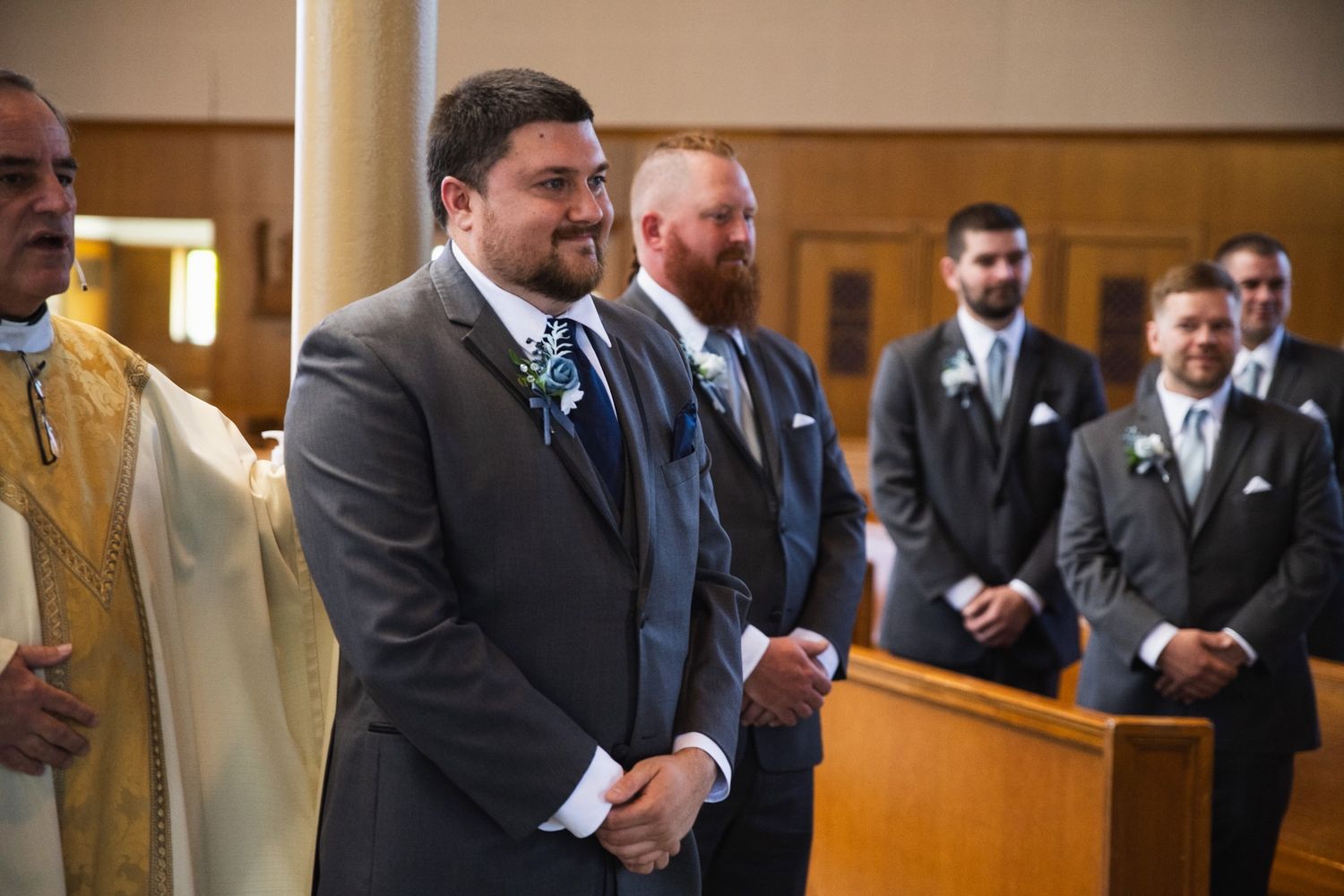 Groomsmen line up at front of church during wedding ceremony in formal attire.
