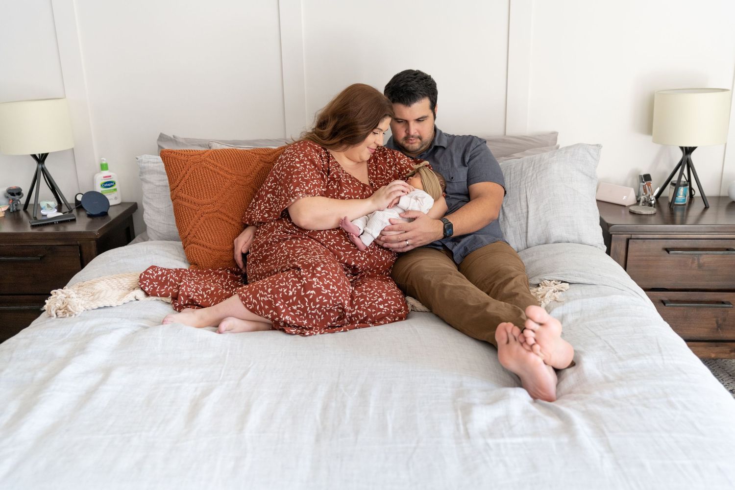 Family relaxing together on a white bed with decorative pillows.