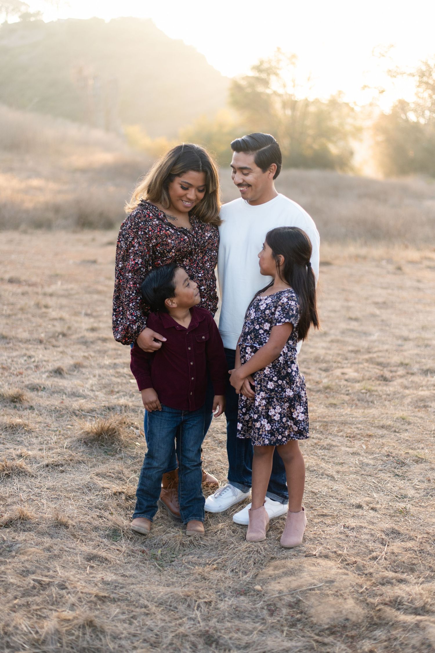 Family of four standing together in casual attire during golden hour photoshoot.