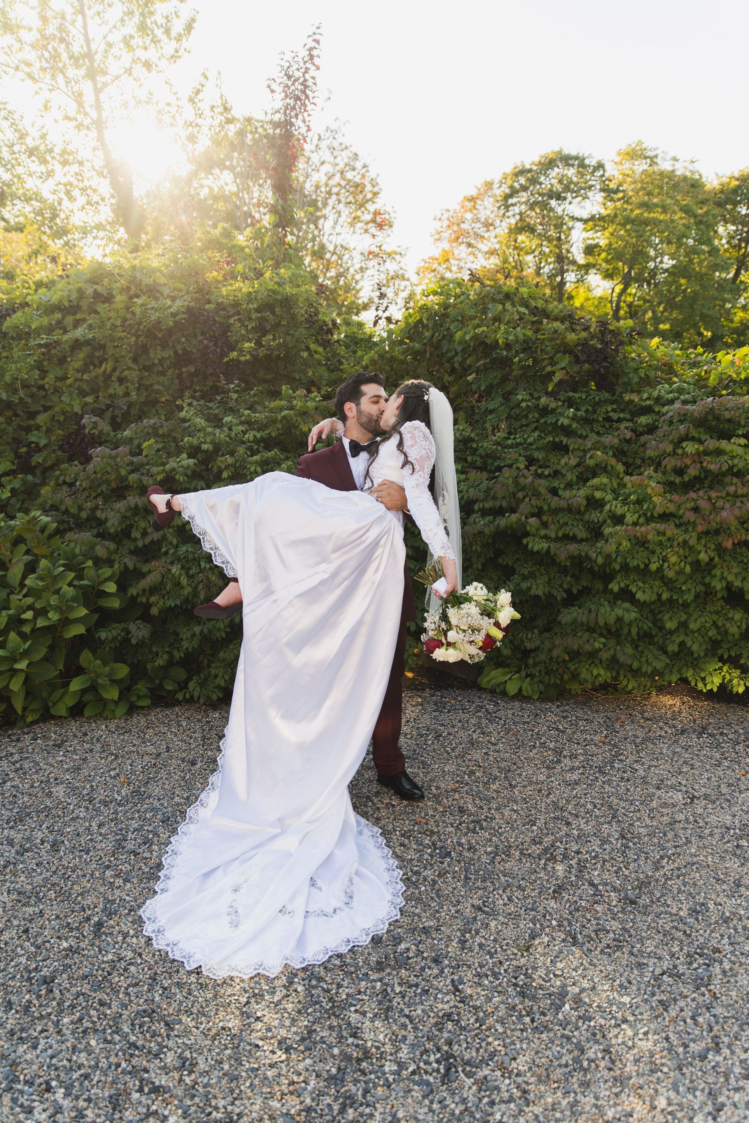 A romantic dance dip pose captured at sunset in a garden setting with gravel ground and green hedges.