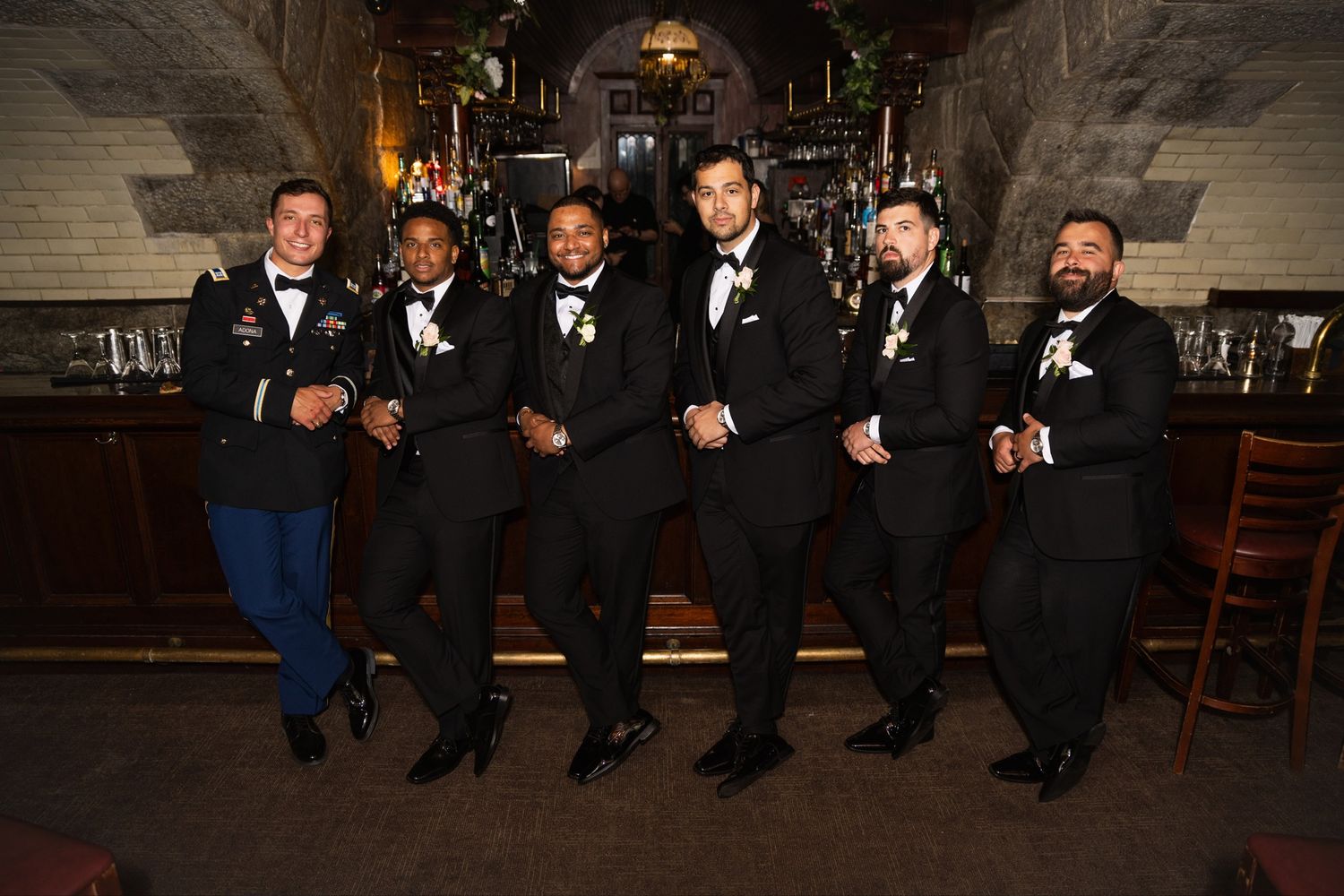 Wedding party in formal attire standing together and laughing against a rustic backdrop.