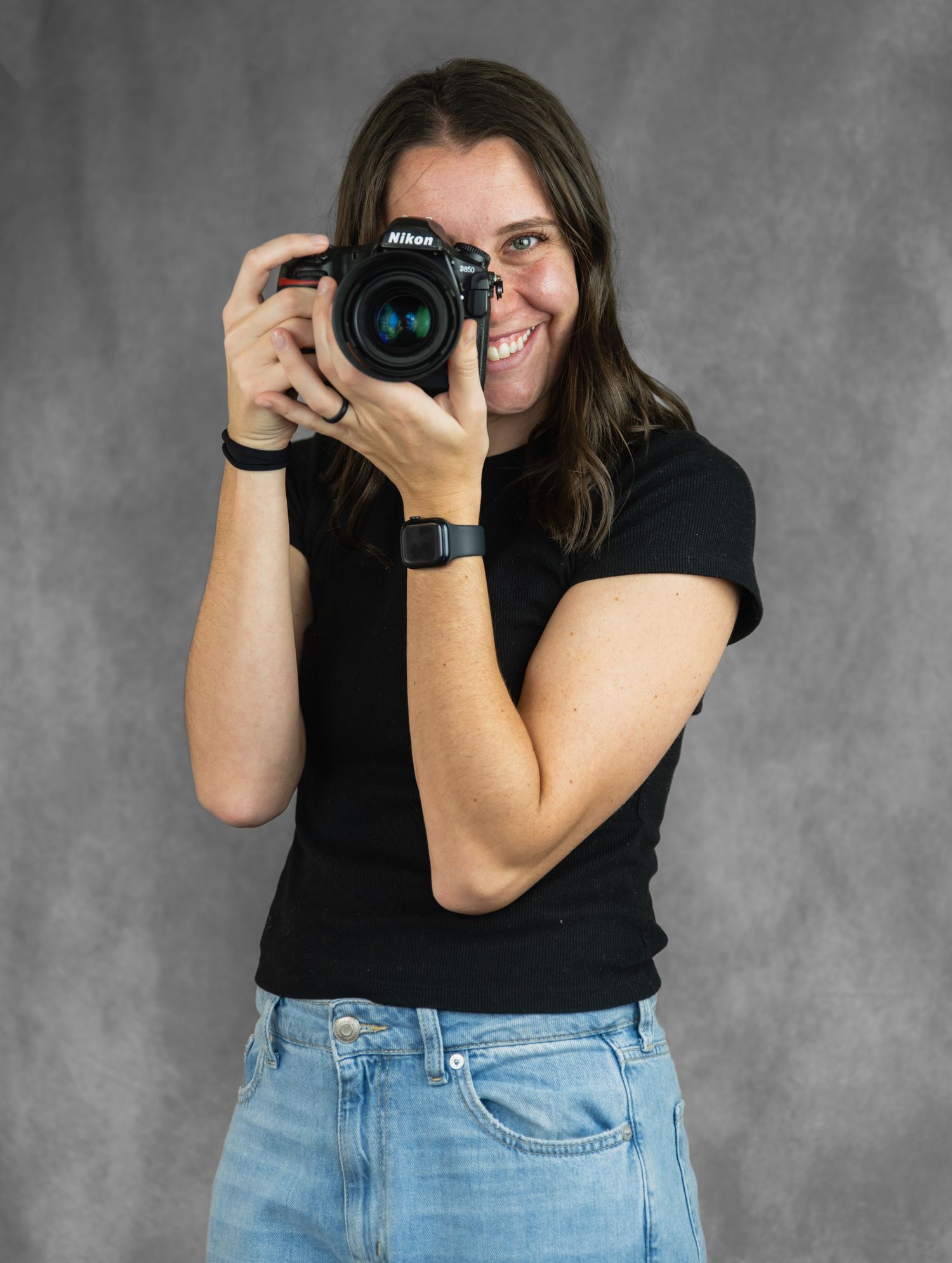 A photographer in a black shirt and jeans poses with a camera against a gray backdrop in a progression of four shots.