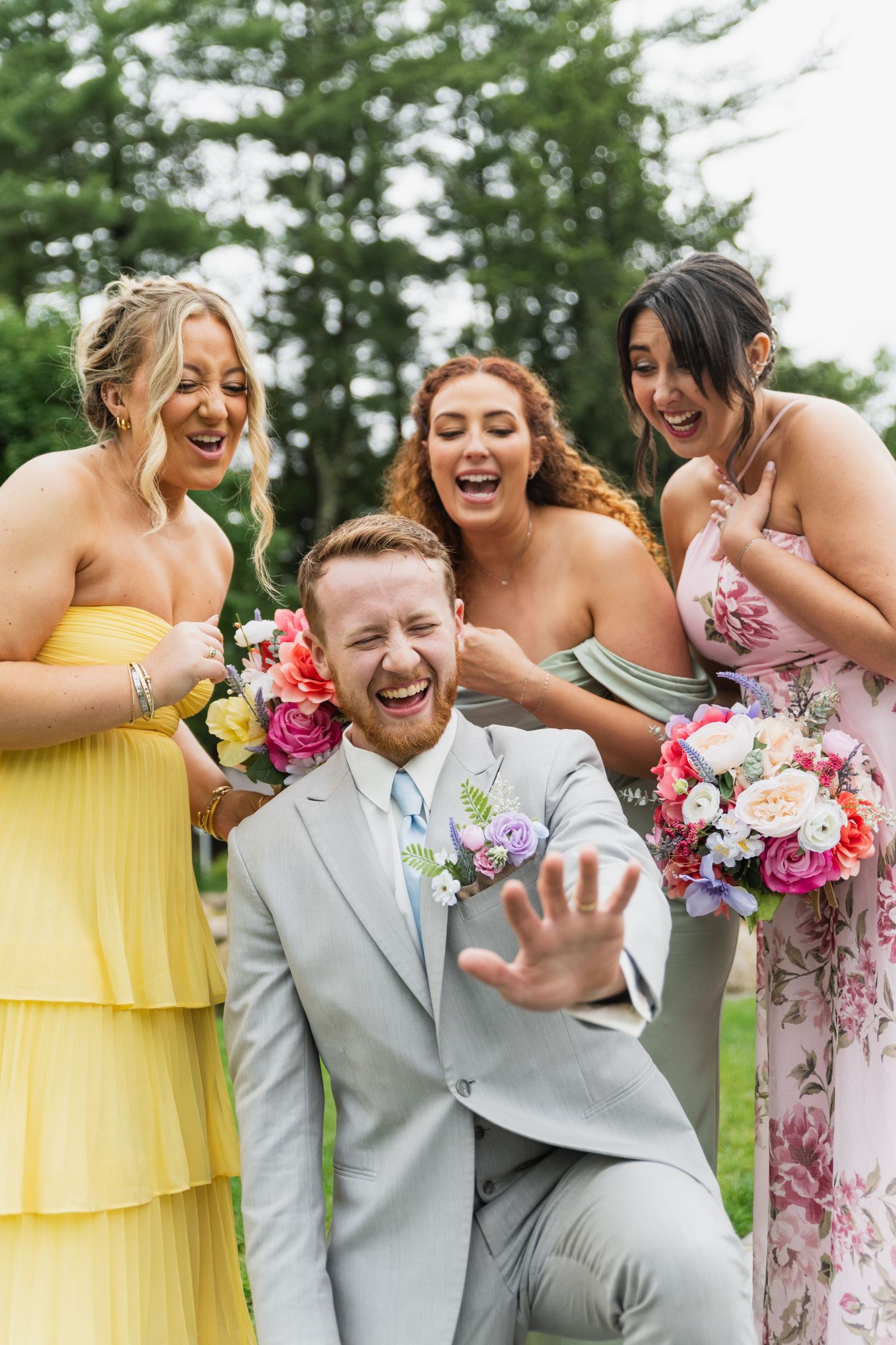 Bridal party in yellow dresses and gray suits laughs together during outdoor photo session.