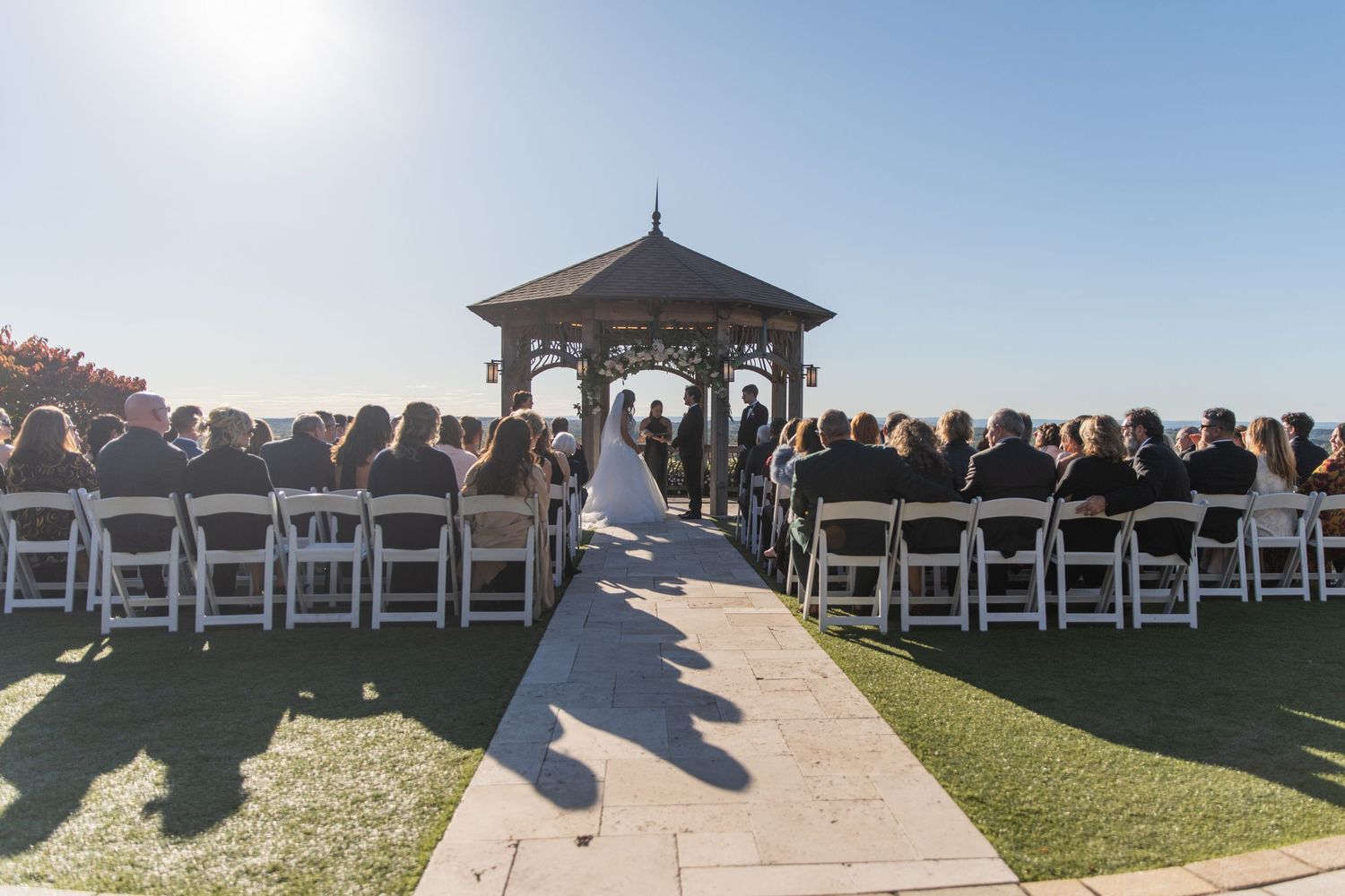 A large crowd gathers at a scenic overlook gazebo during sunset to enjoy panoramic coastal views.