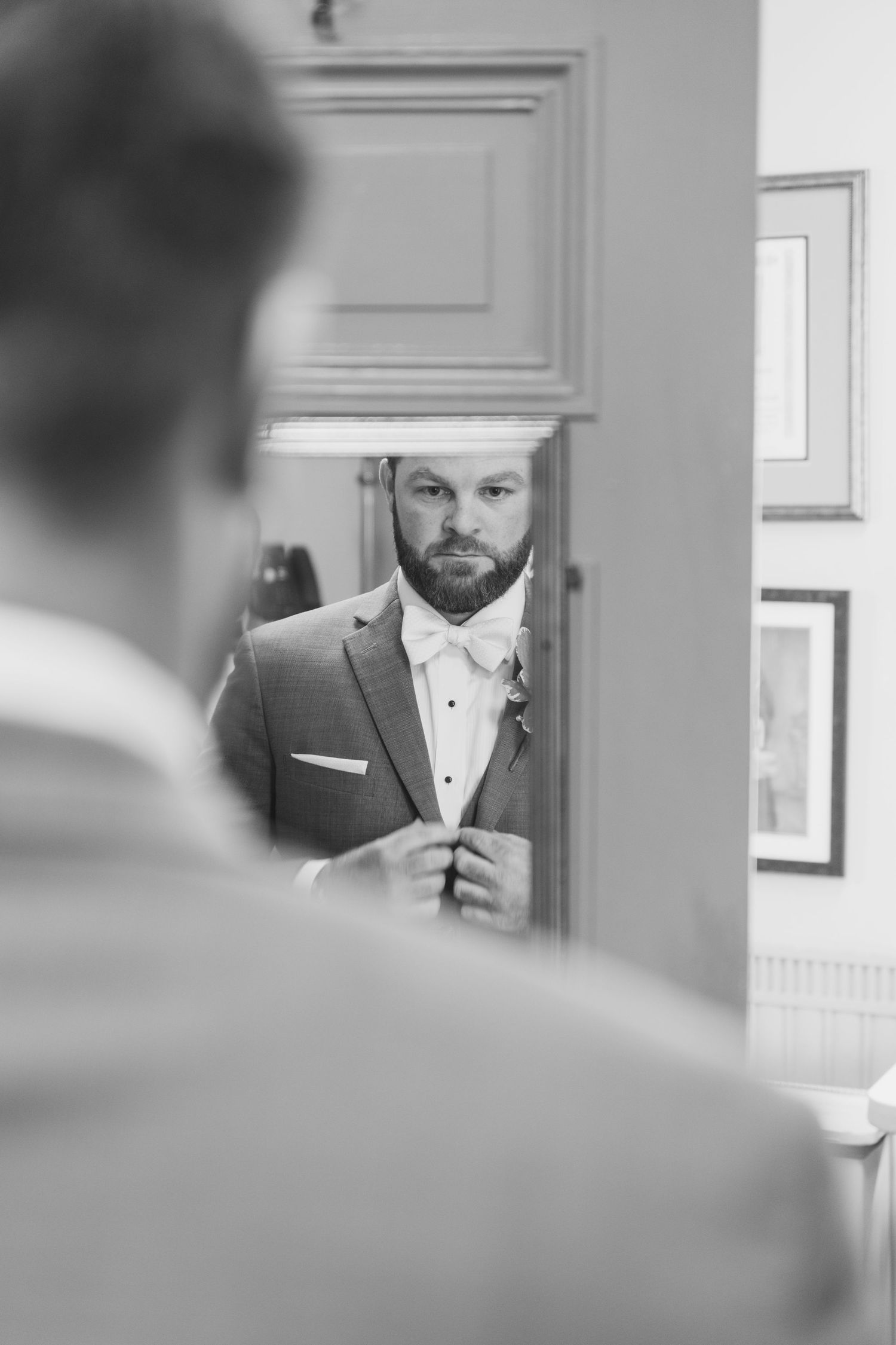 Black and white image of formal attire adjustments in a mirror.