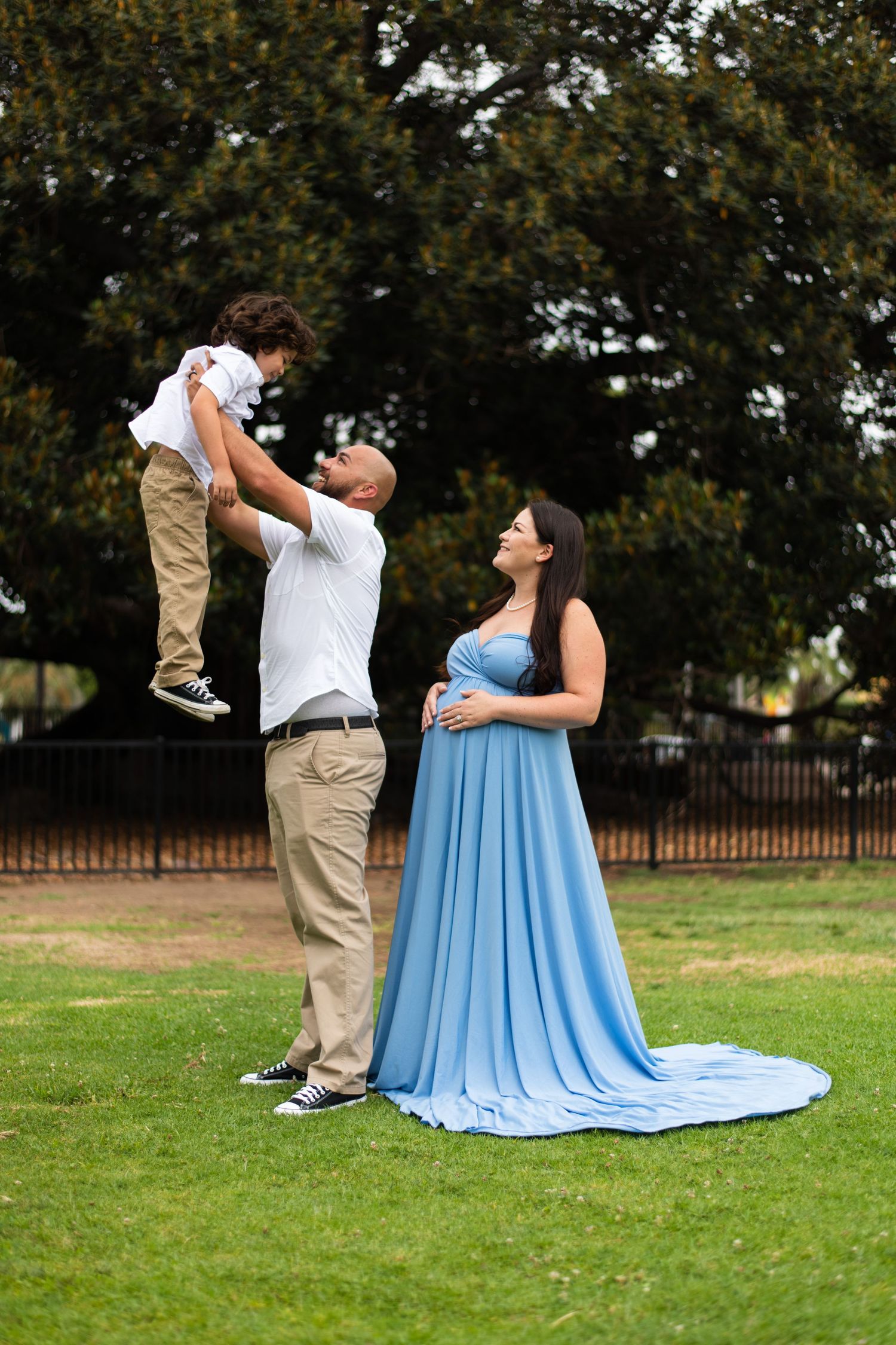Family maternity photo session on green lawn showing playful interactions.