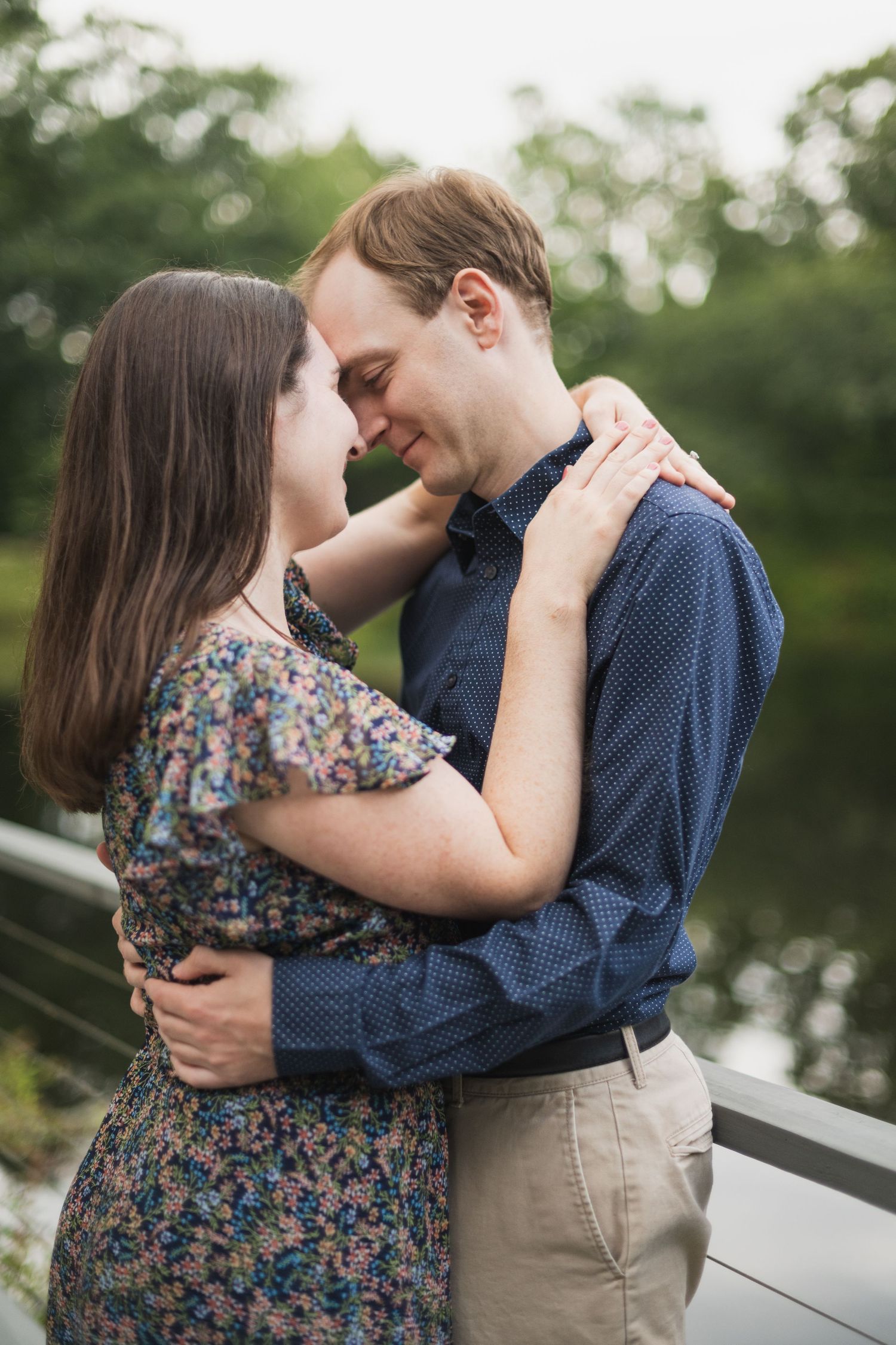 Two people share an intimate moment while embracing on a deck overlooking nature.