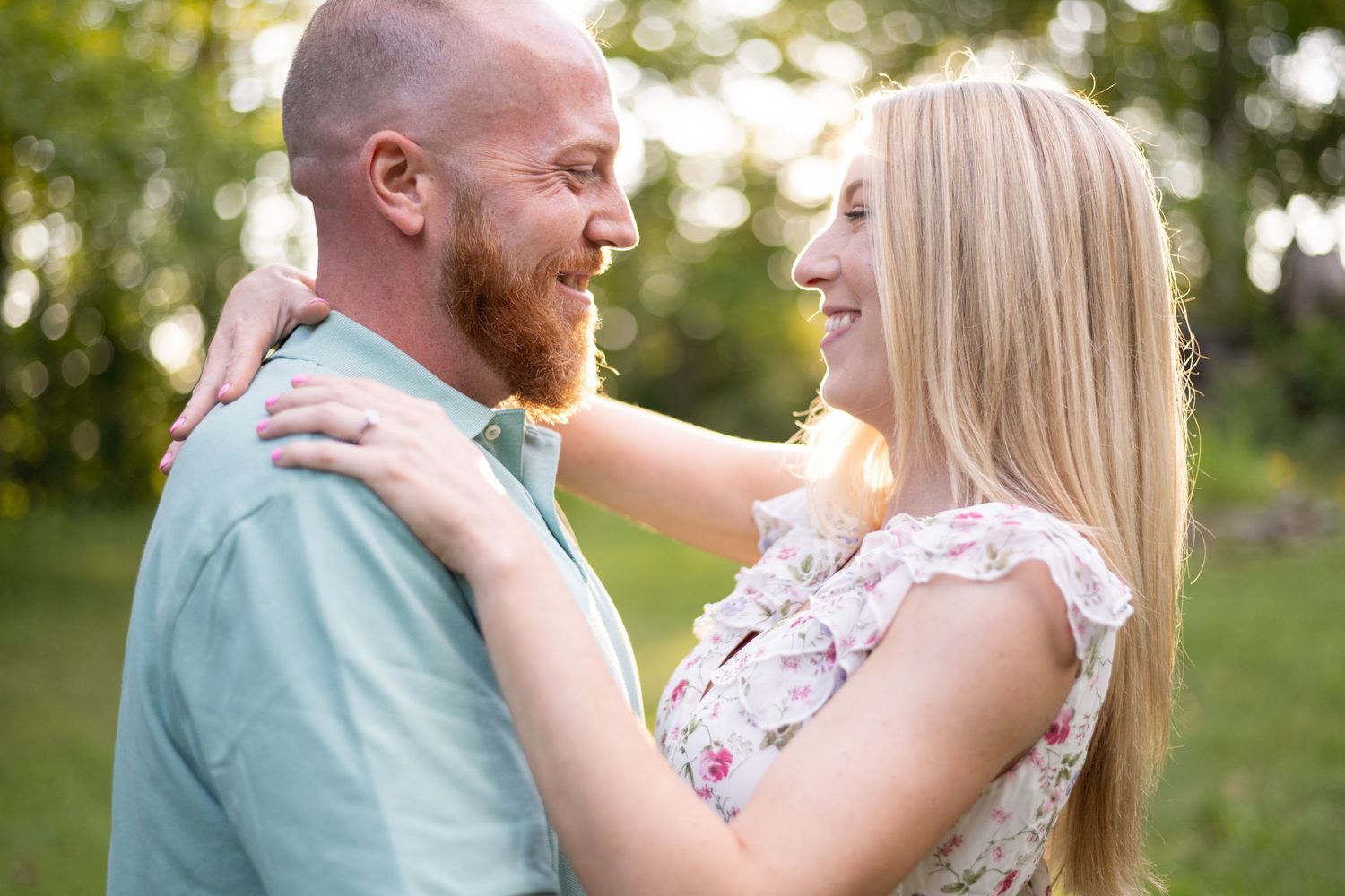 Romantic couple shares intimate moment in outdoor setting with sunlit trees in background.