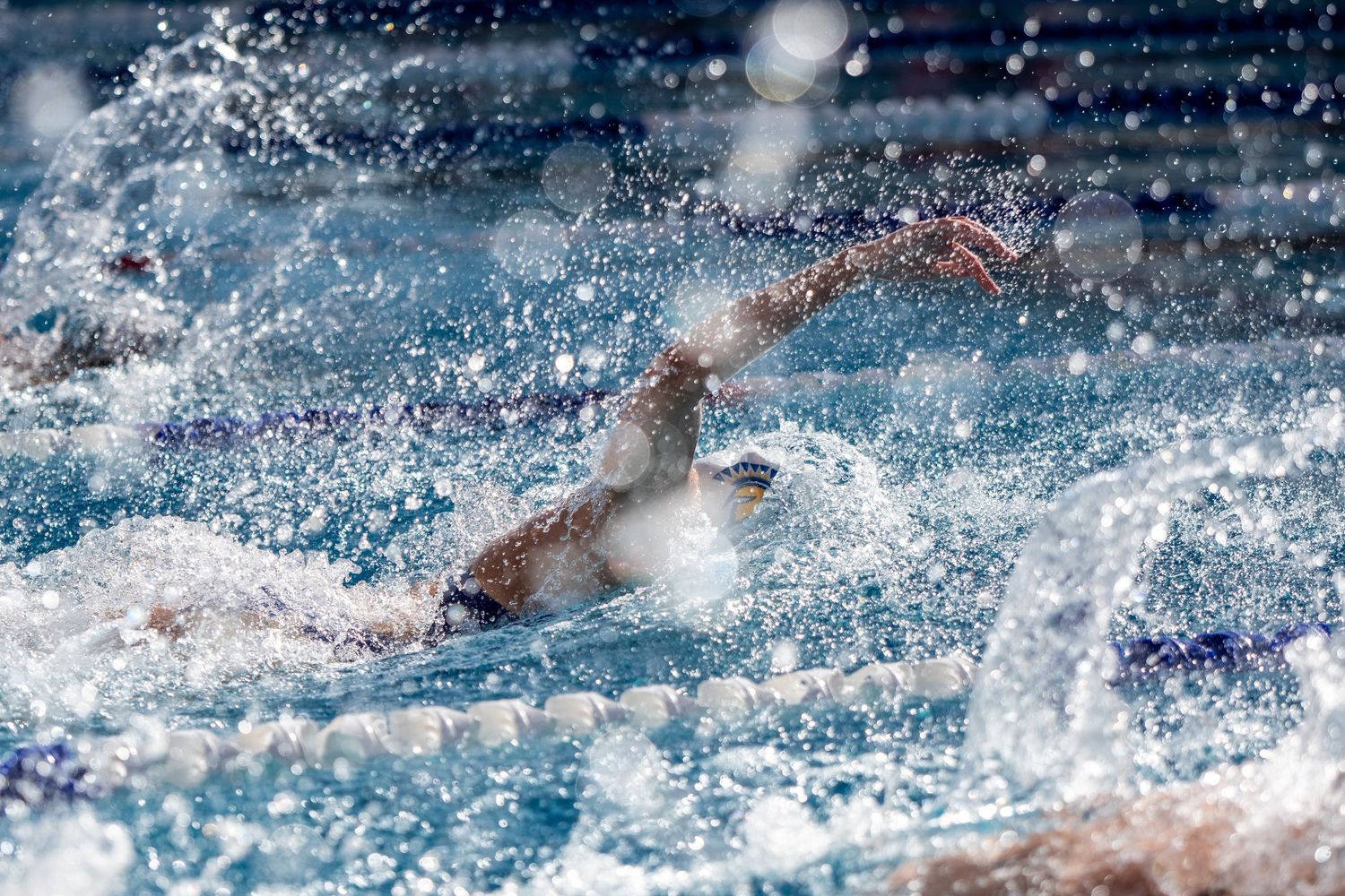 Competitive swimmer performing freestyle stroke in a splashing pool during a swim race.