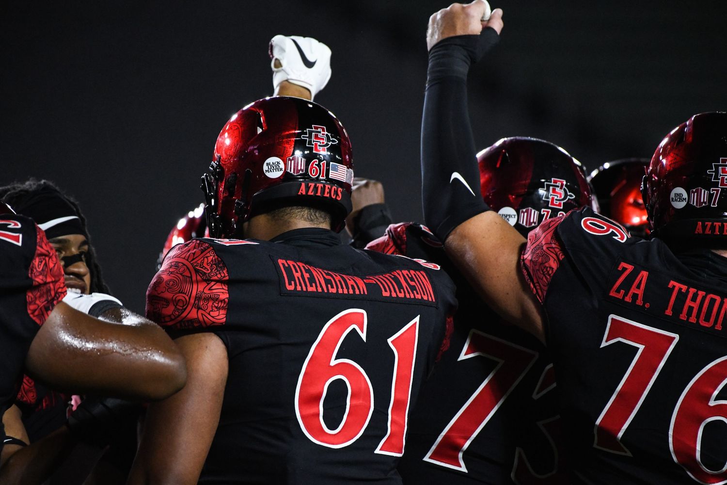 San Diego State Aztecs football players huddle together on field wearing red jerseys during a night game.