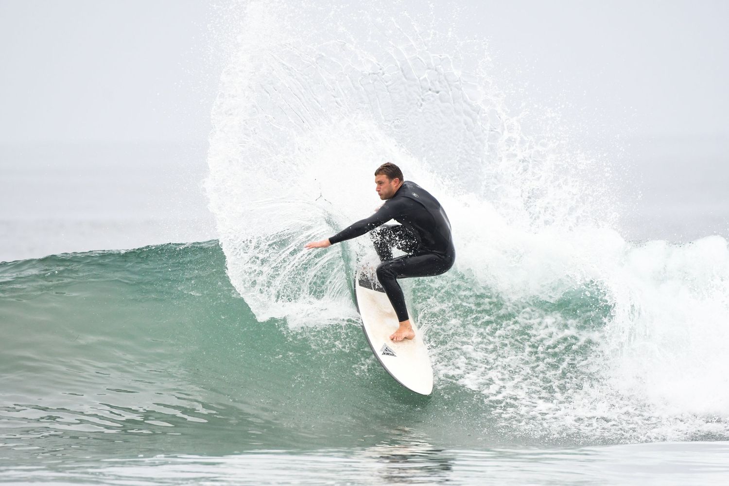Surfer in black wetsuit riding a wave on a white surfboard in the ocean on a cloudy day.