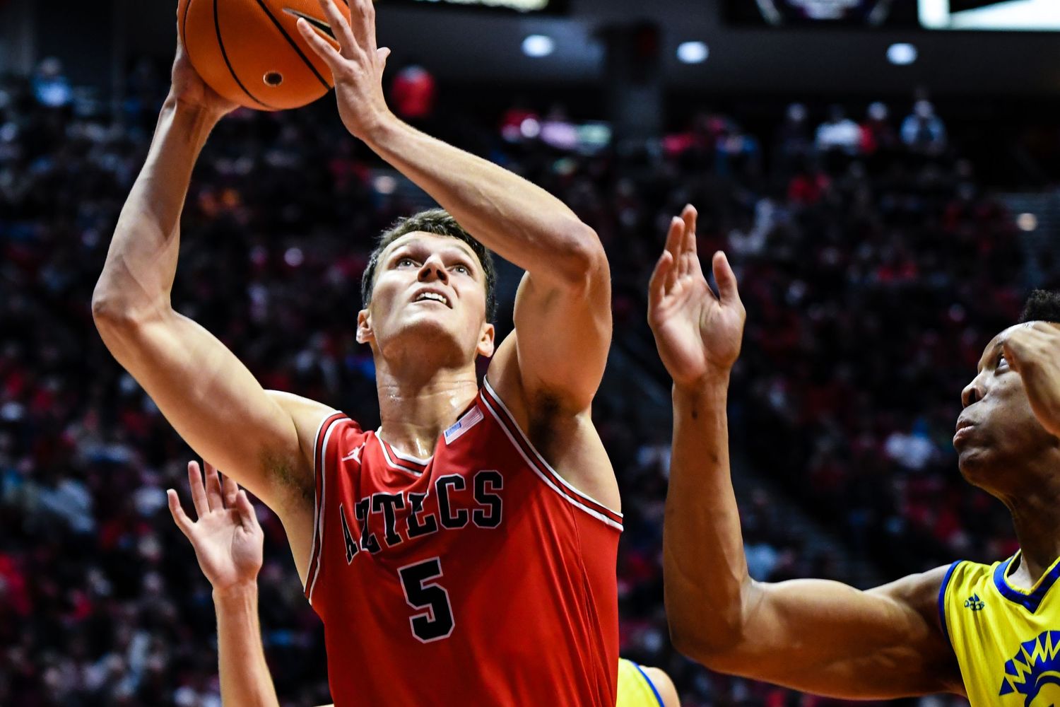 San Diego State Aztecs player #5 drives to the basket during a college basketball game against a team in yellow uniforms.