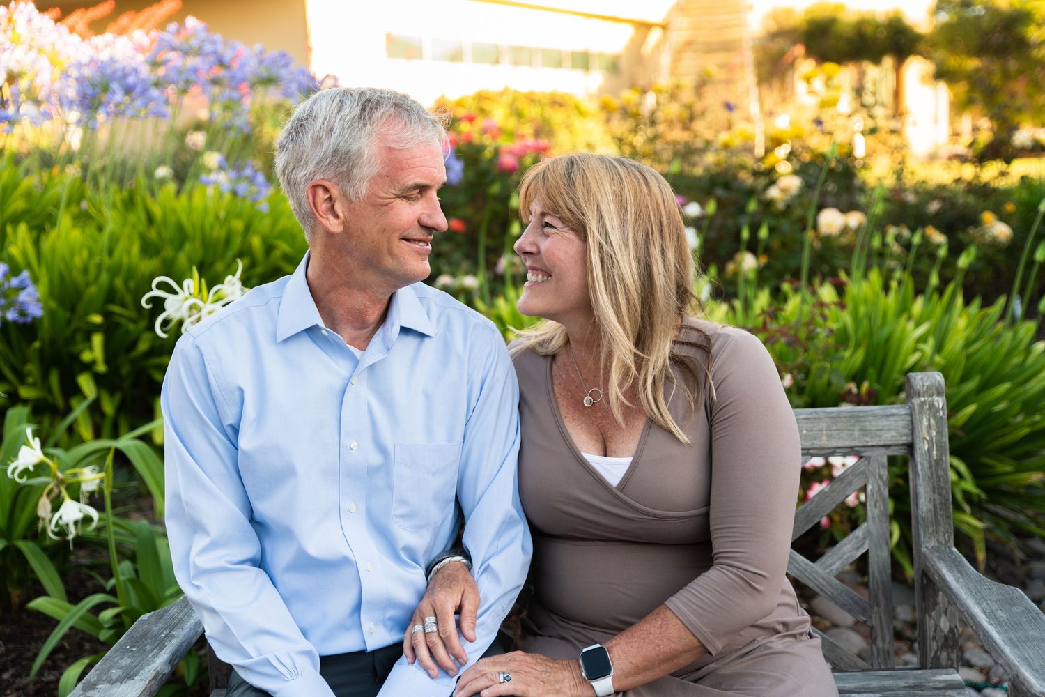 Mature couple sharing tender moment while sitting on garden bench surrounded by flowers.