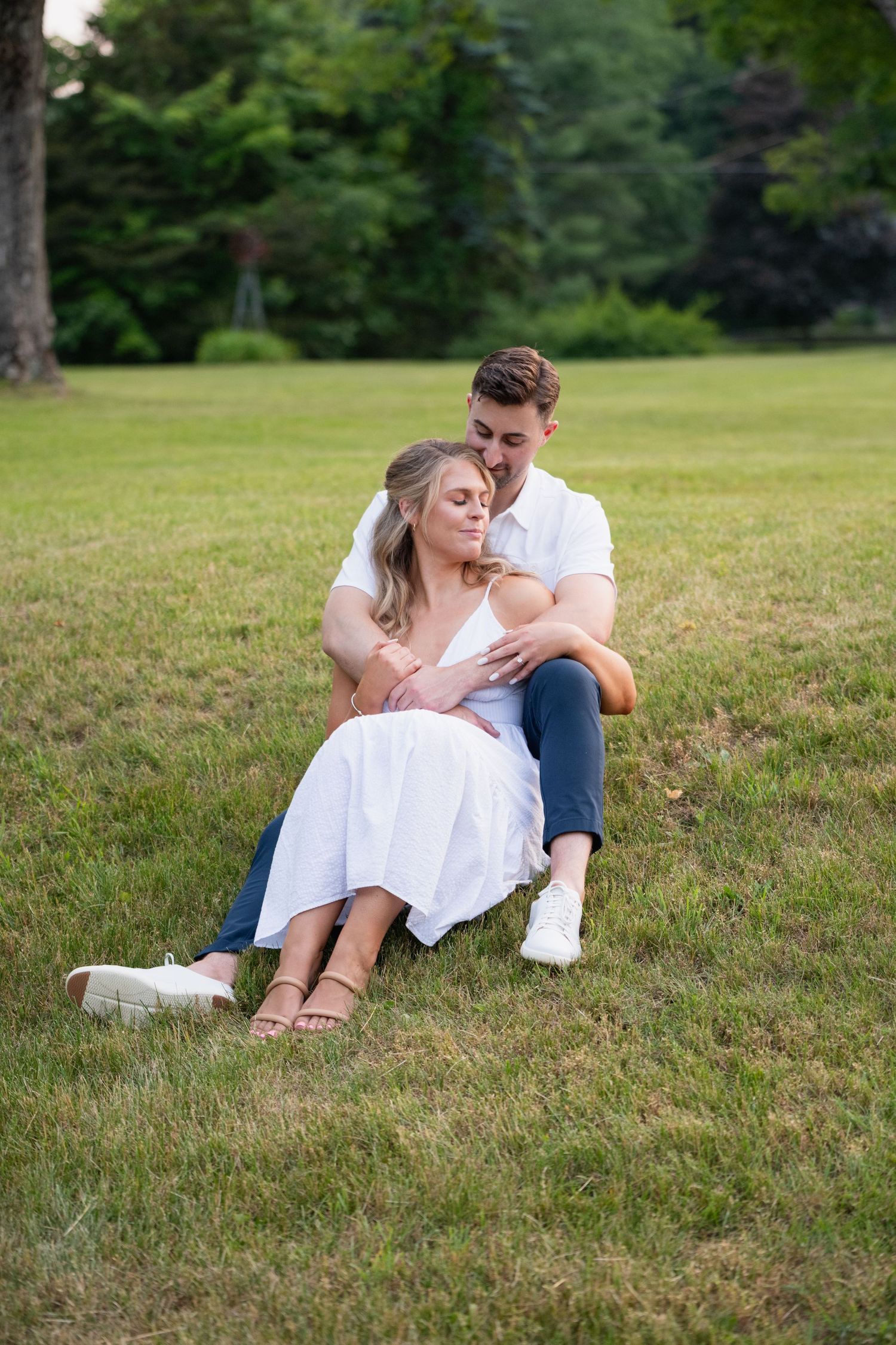 A romantic couple relaxes together on a grassy hillside during a summer photoshoot.