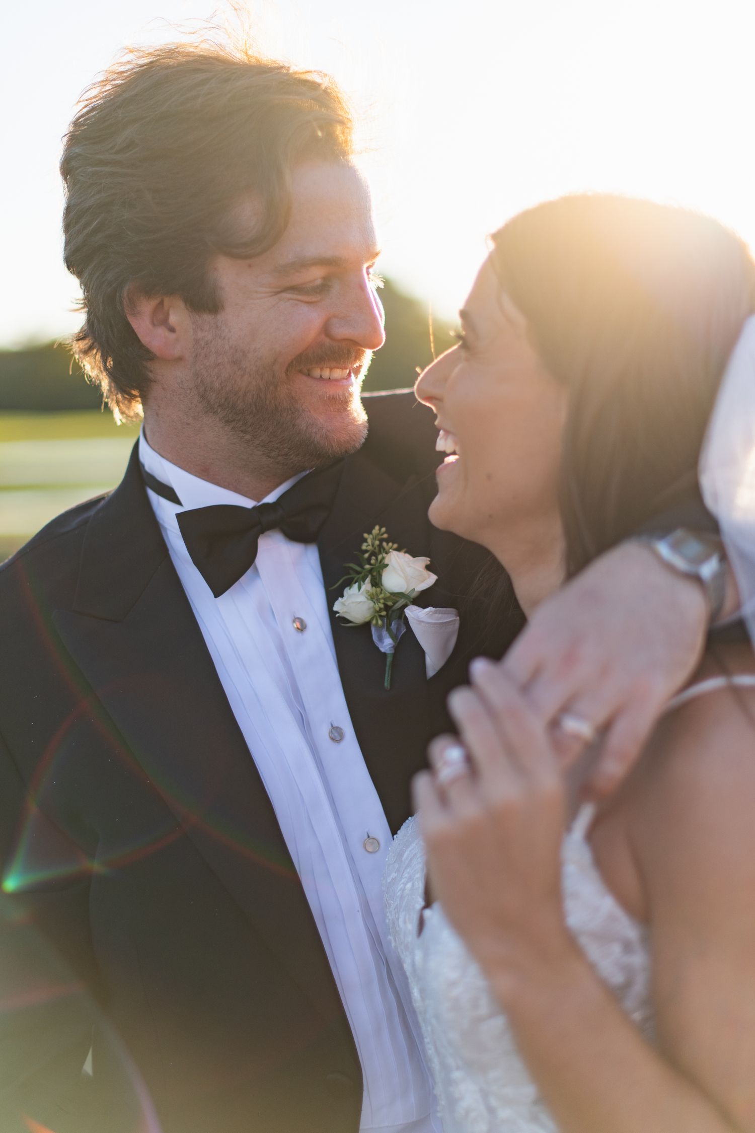 A romantic wedding couple shares an intimate moment at sunset with lens flare creating a dreamy atmosphere.