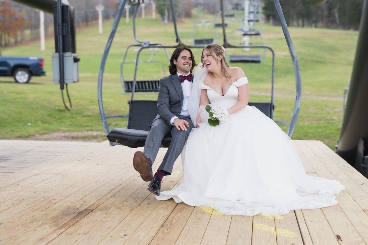 Wedding couple poses together on a wooden swing set in an outdoor setting.