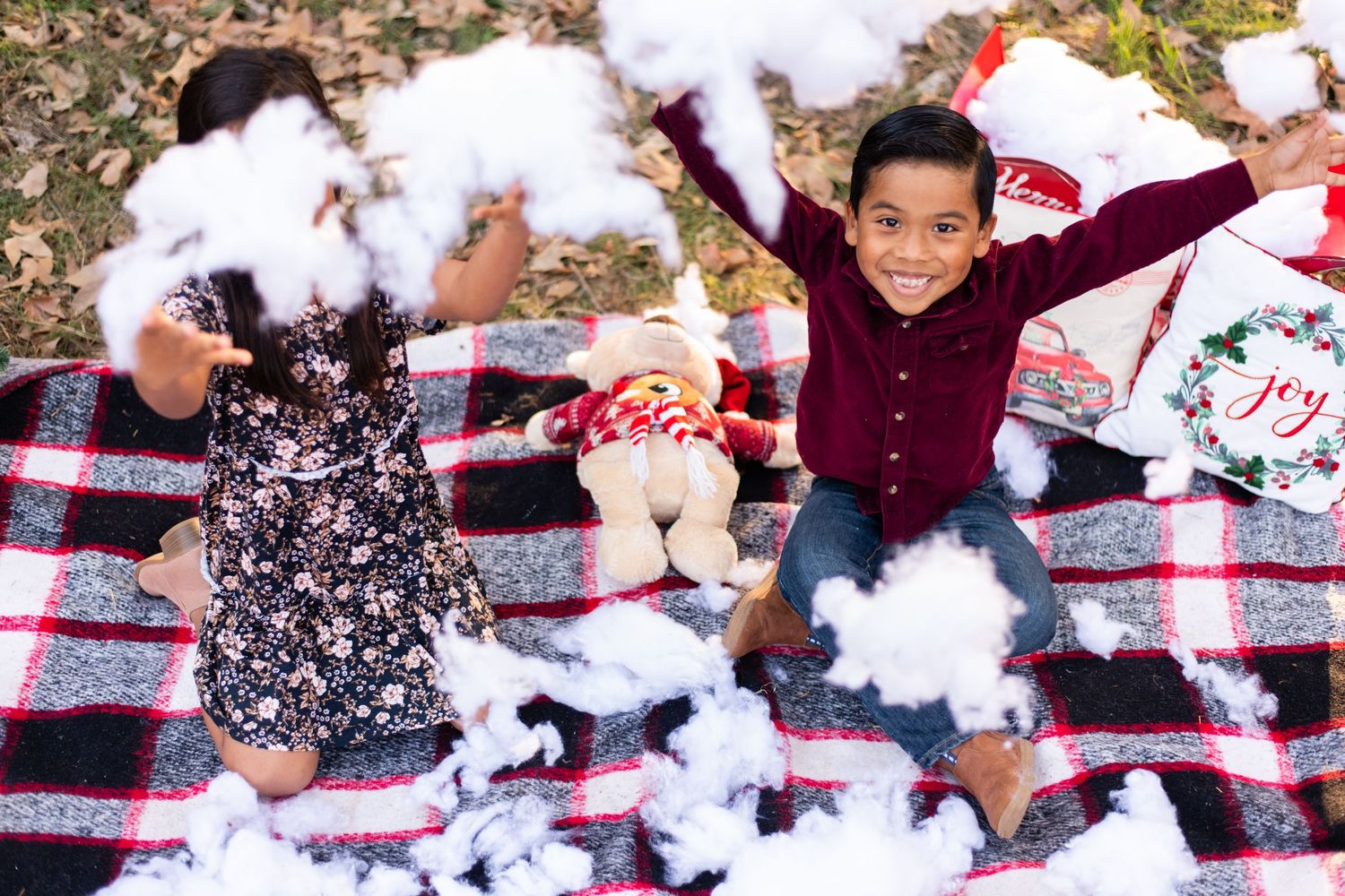 Children having fun playing with cotton fluff on a picnic blanket outdoors.