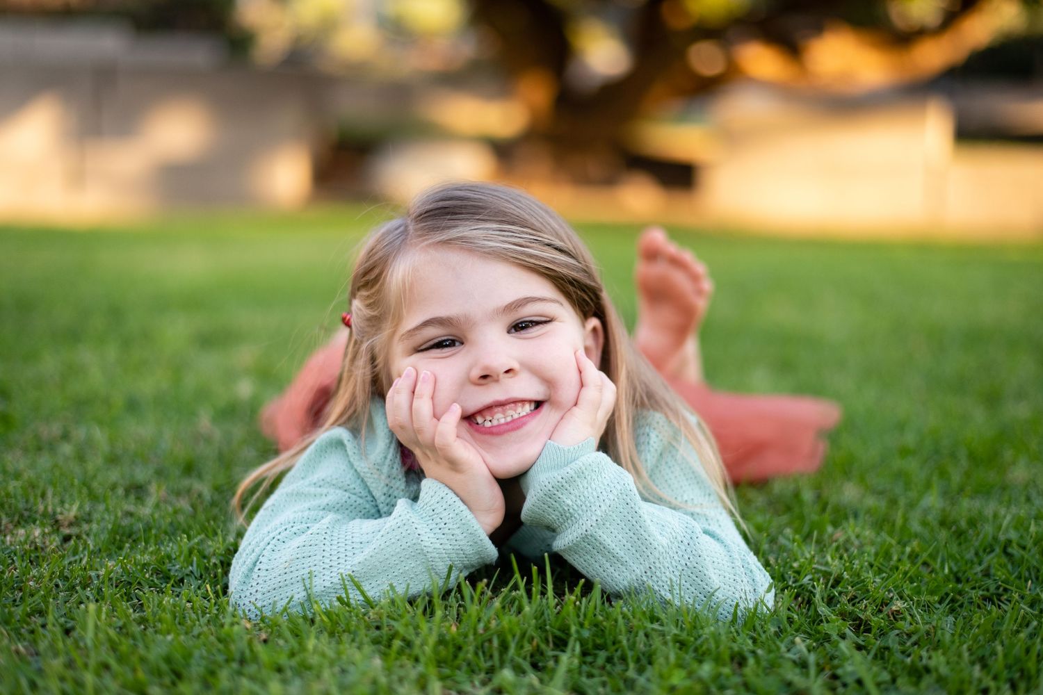 Child laying on grass with hands under chin during golden hour.