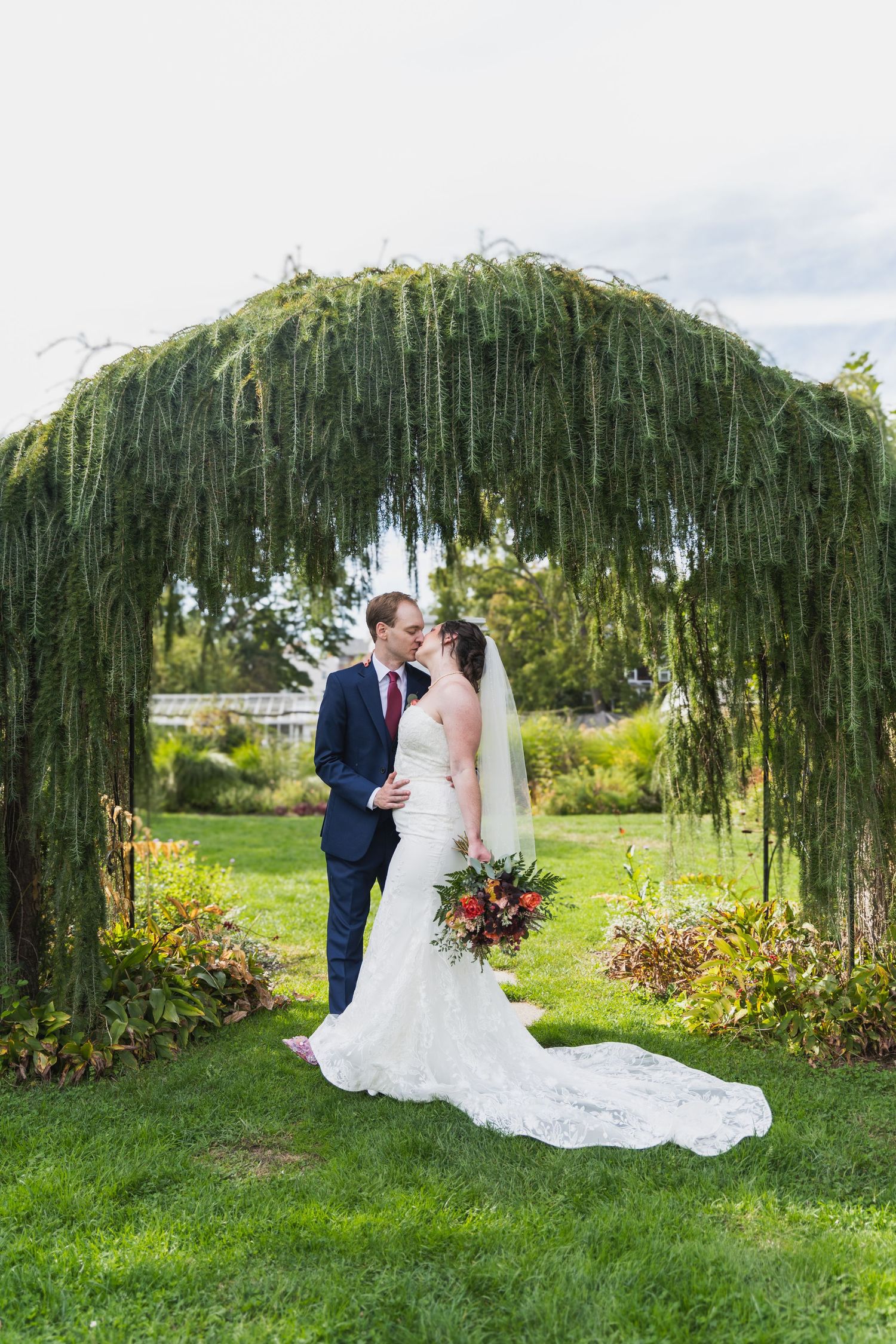 Wedding couple poses for romantic portraits under a weeping willow tree in a garden setting.