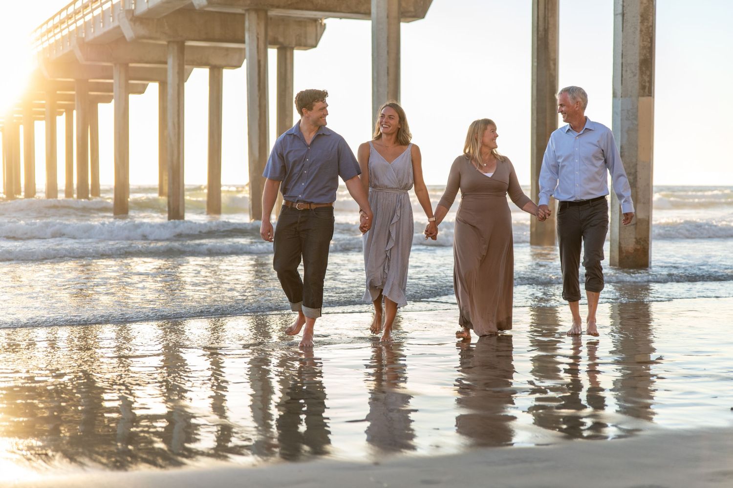 Silhouettes of people walking along a beach pier at golden hour.