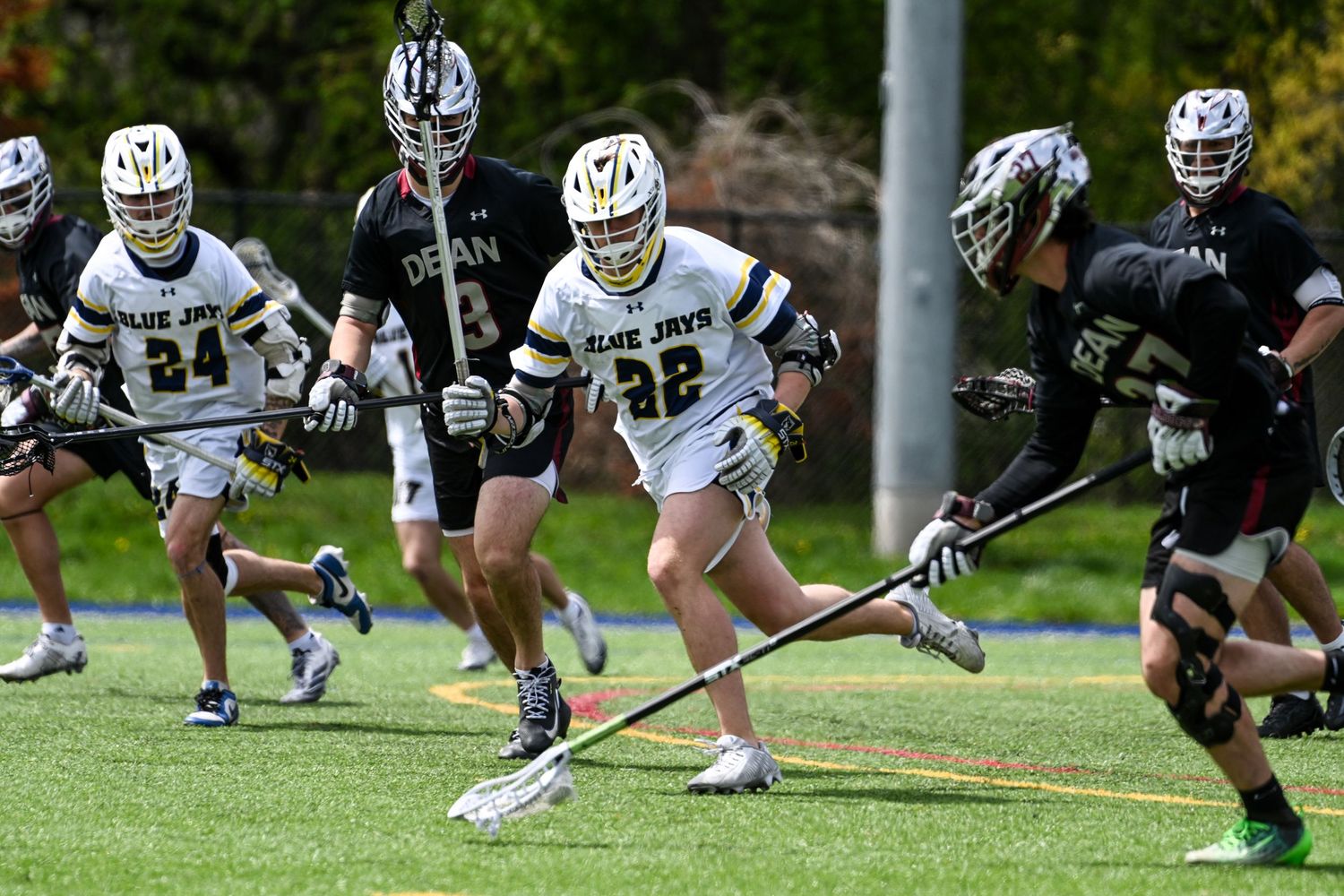 Blue Jays lacrosse players in white and gold uniforms compete against opponents in a field game.