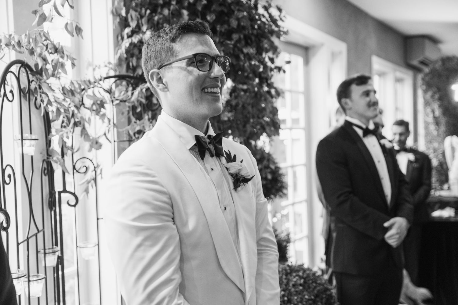Wedding party members stand in formal attire on a porch with decorative iron details.