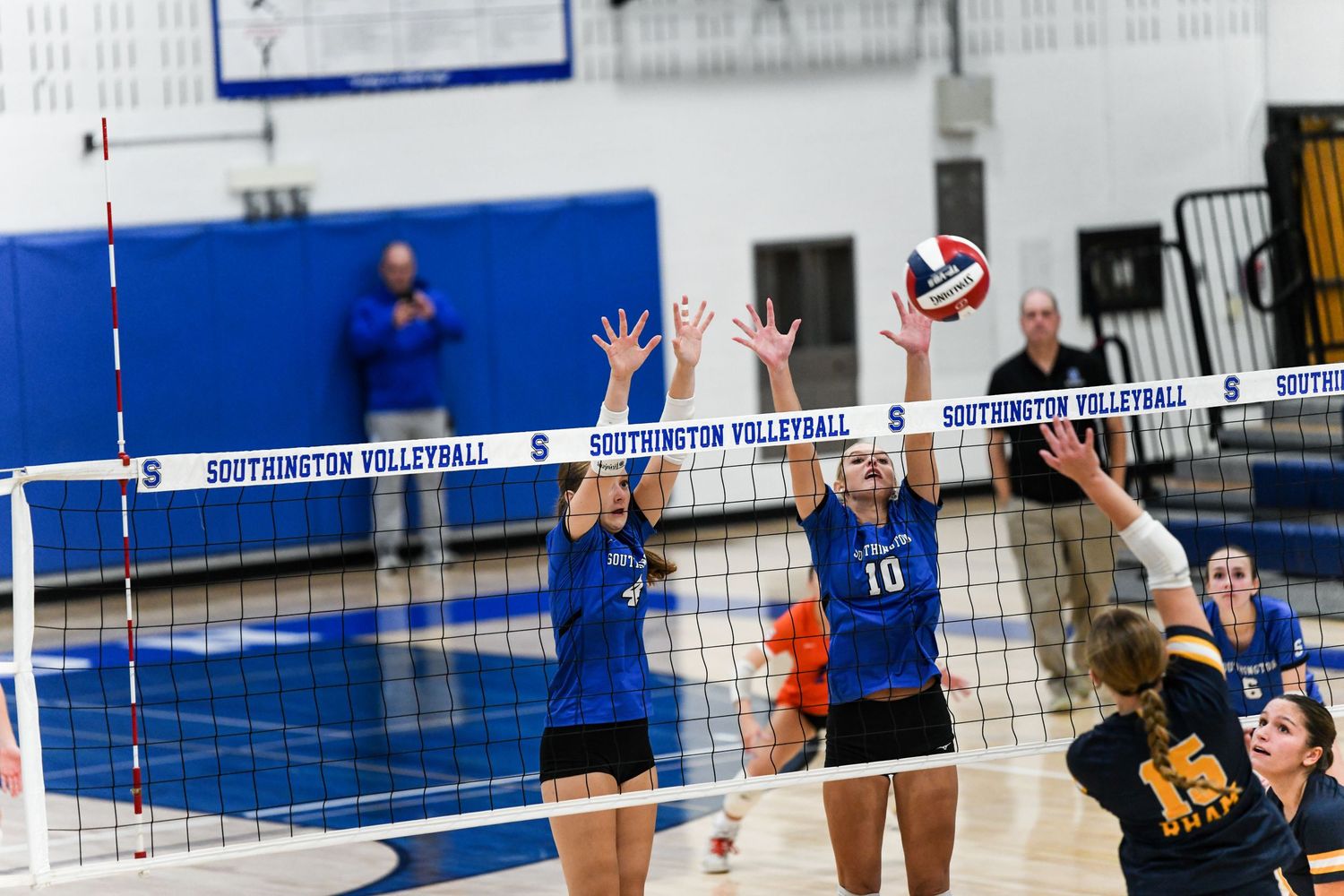 Two volleyball players in blue uniforms jump to block a spike at the net during a Southington Volleyball match.
