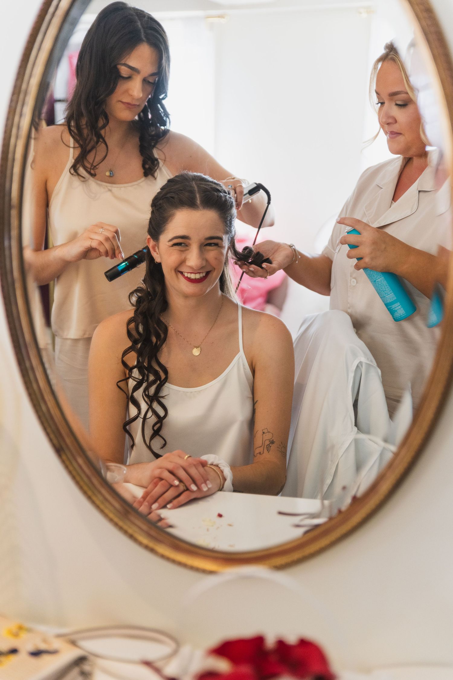 Mirror reflections show bridal party getting ready with hair styling and makeup preparations.