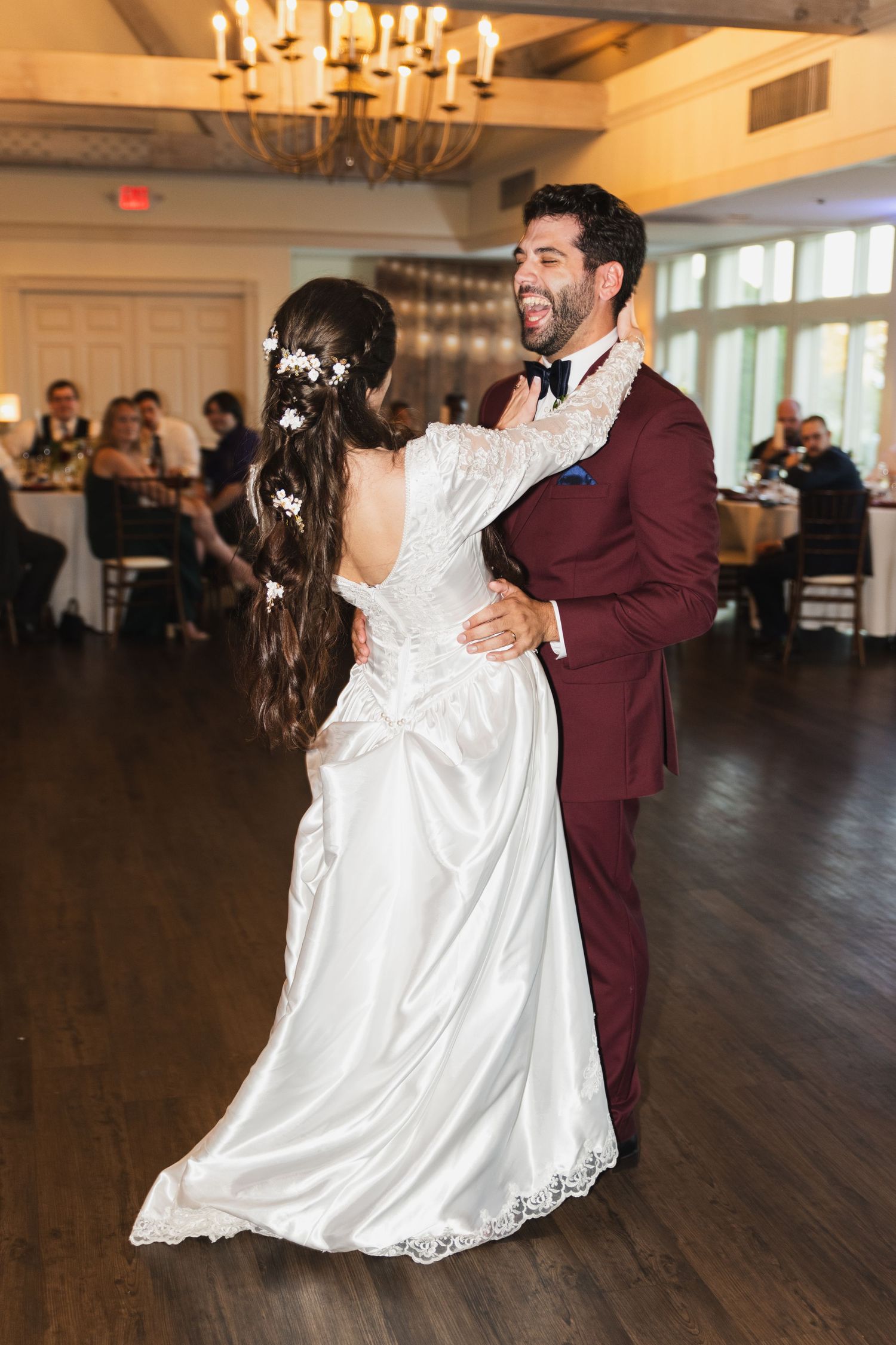 Couple shares romantic first dance in elegant ballroom with chandelier lighting.