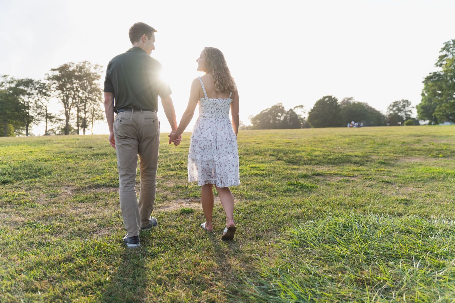 Silhouetted couple walking hand in hand through a grassy field at sunset.