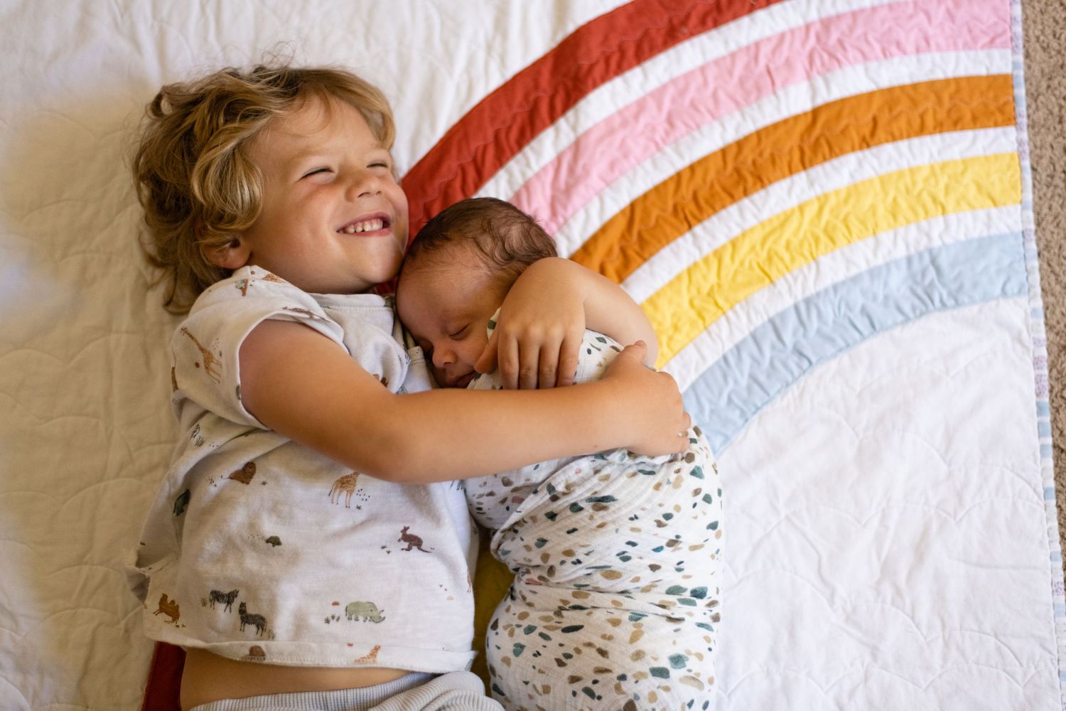 Rainbow-striped blanket serves as backdrop for a tender bonding moment on white sheets.