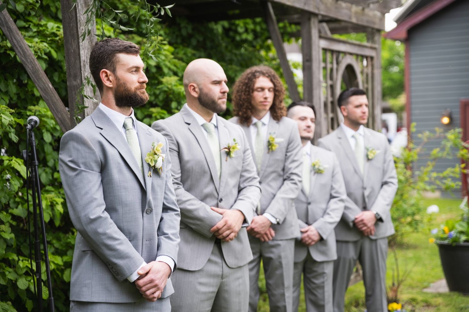 Groomsmen in matching gray suits standing in a line outdoors.