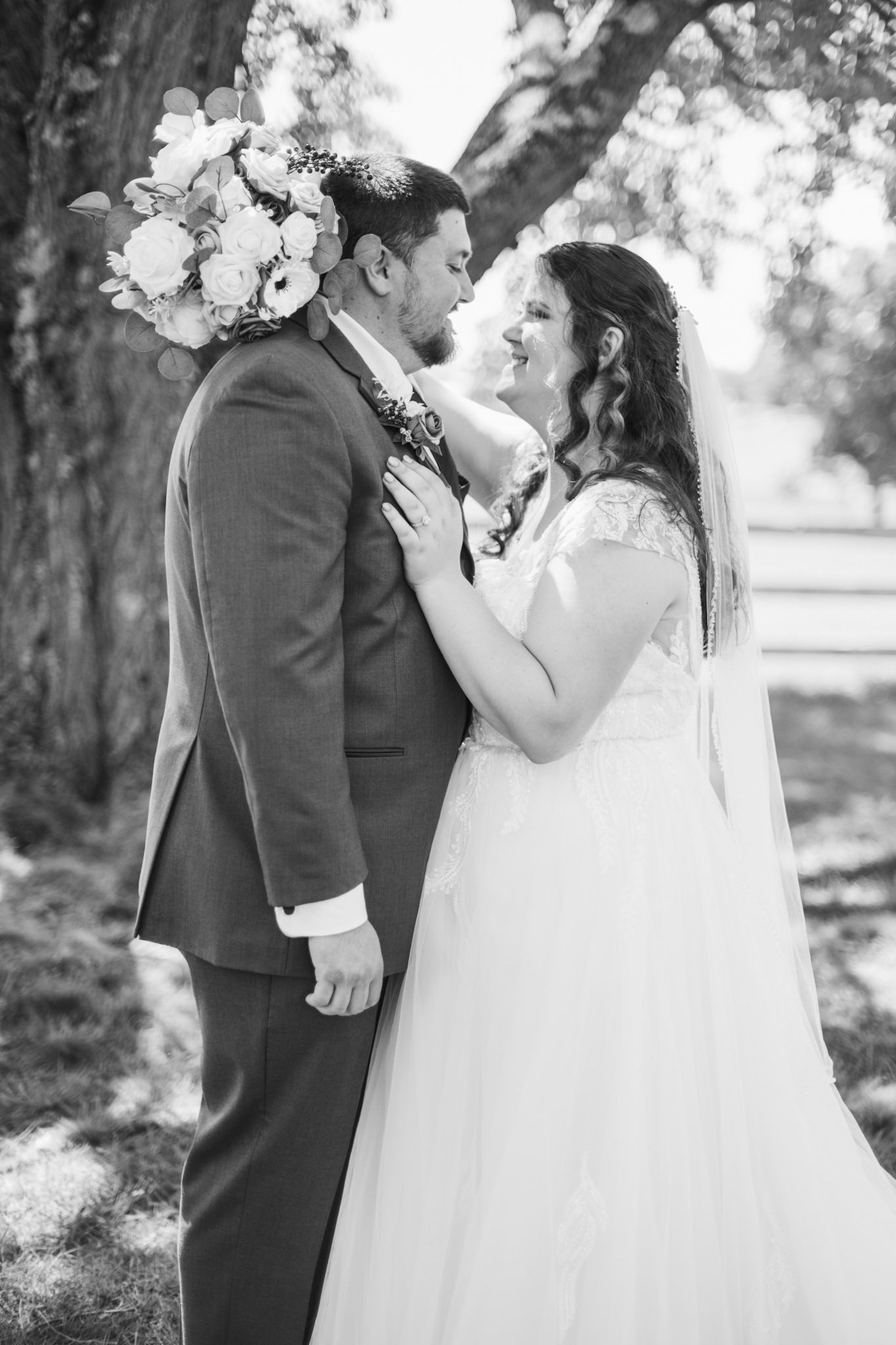 A romantic black and white wedding photo of a couple embracing under a tree with floral decorations.