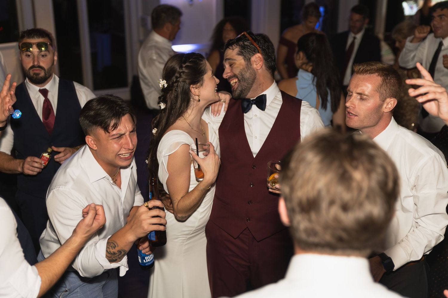 Wedding reception guests dancing and celebrating on a dark dance floor with party lights.