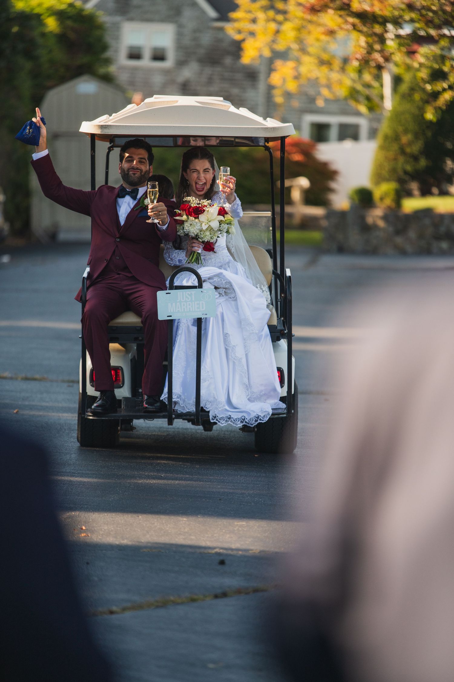 A couple rides in a golf cart decorated for a wedding celebration with white dress flowing behind.