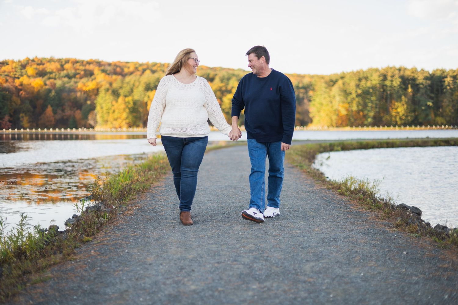 Couple walking along waterfront path during beautiful autumn sunset.