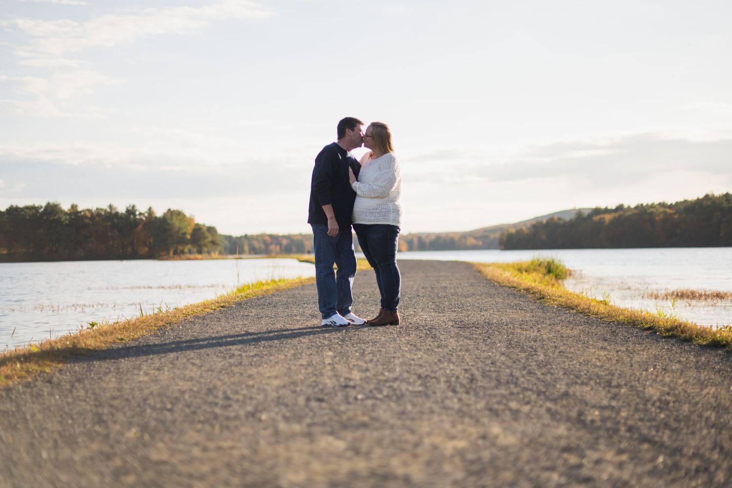 Silhouetted figures embrace on waterfront path during sunset.