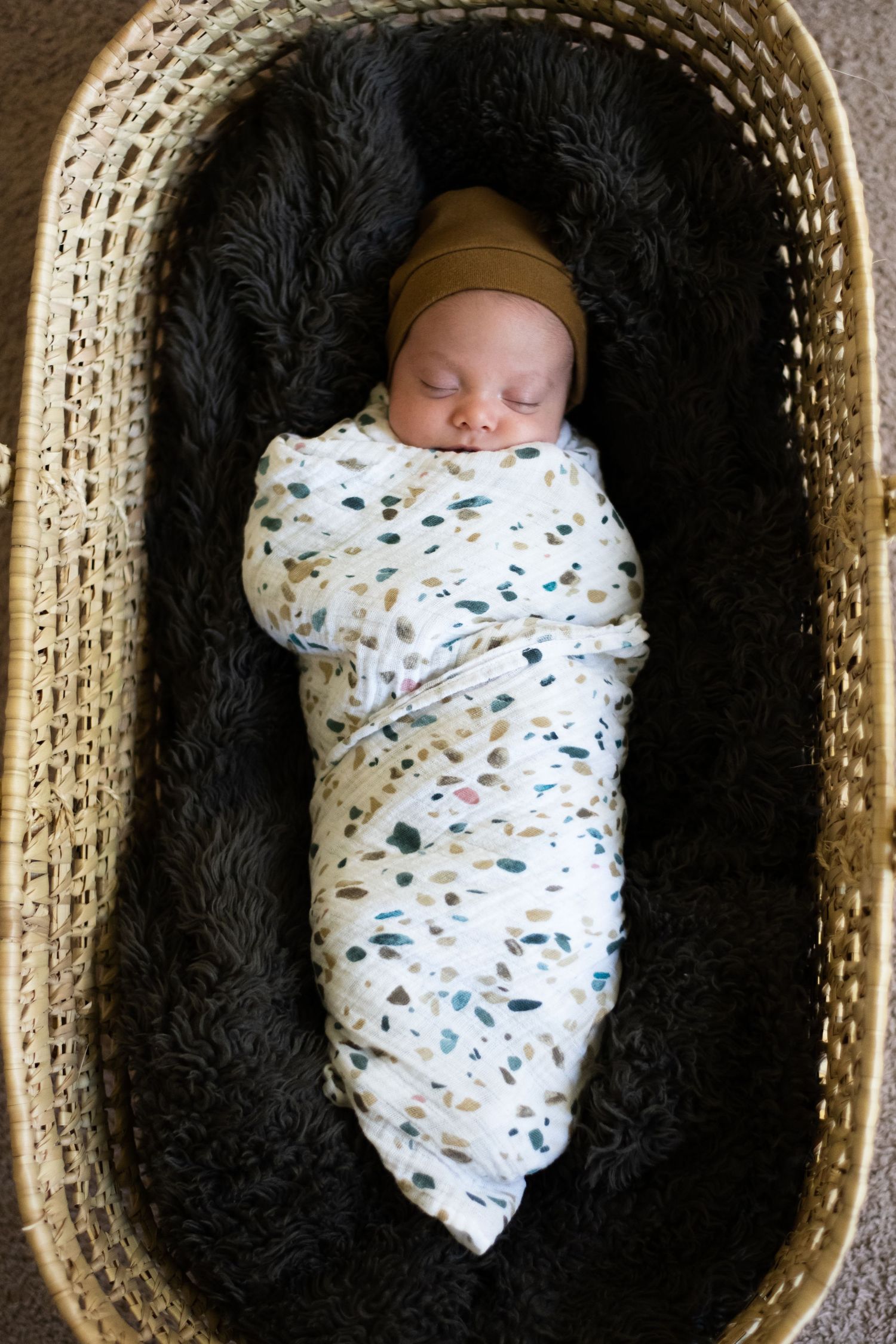 Sleeping newborn swaddled in patterned blanket in woven basket.
