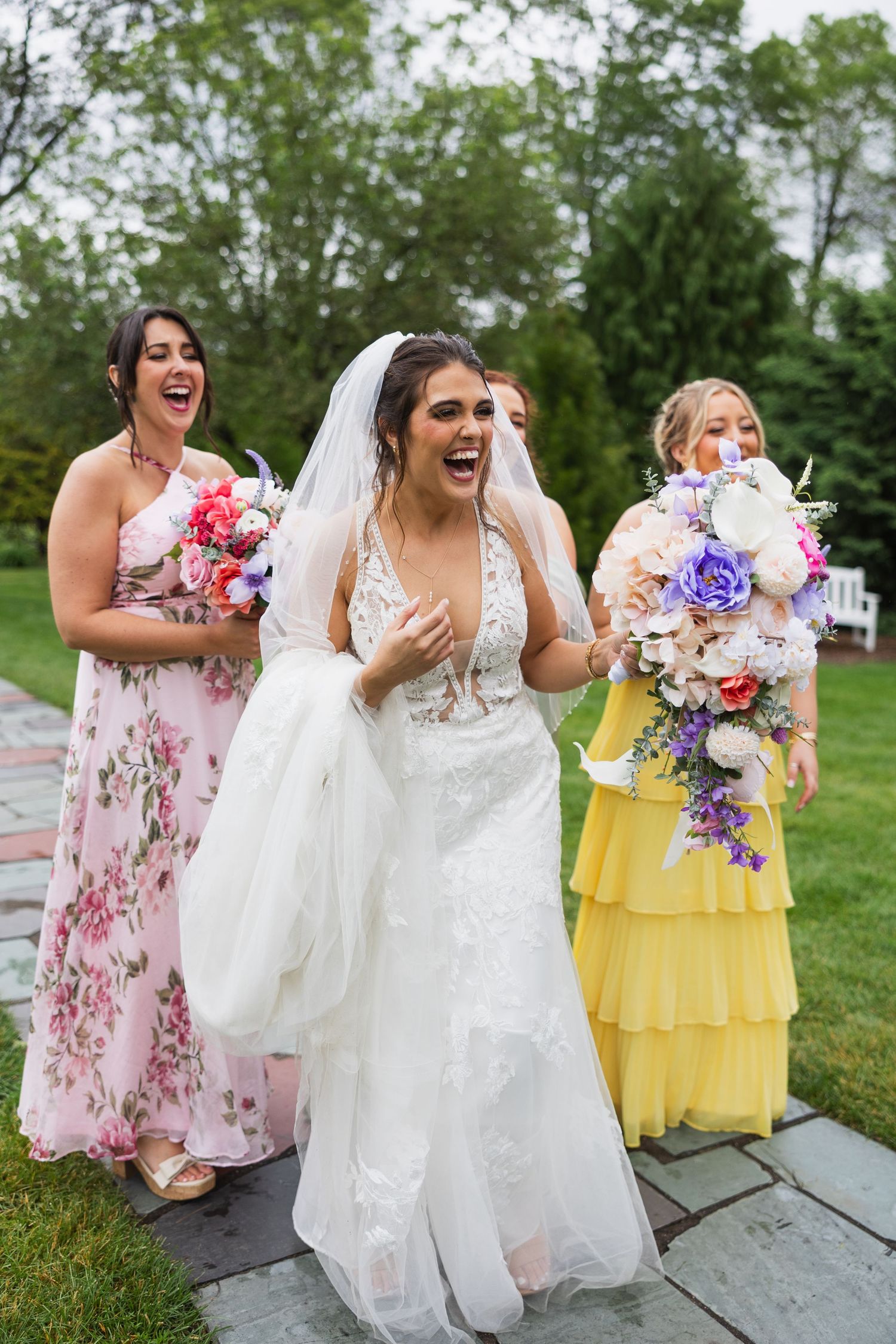 Bridal party in floral and yellow dresses laughing together outdoors.