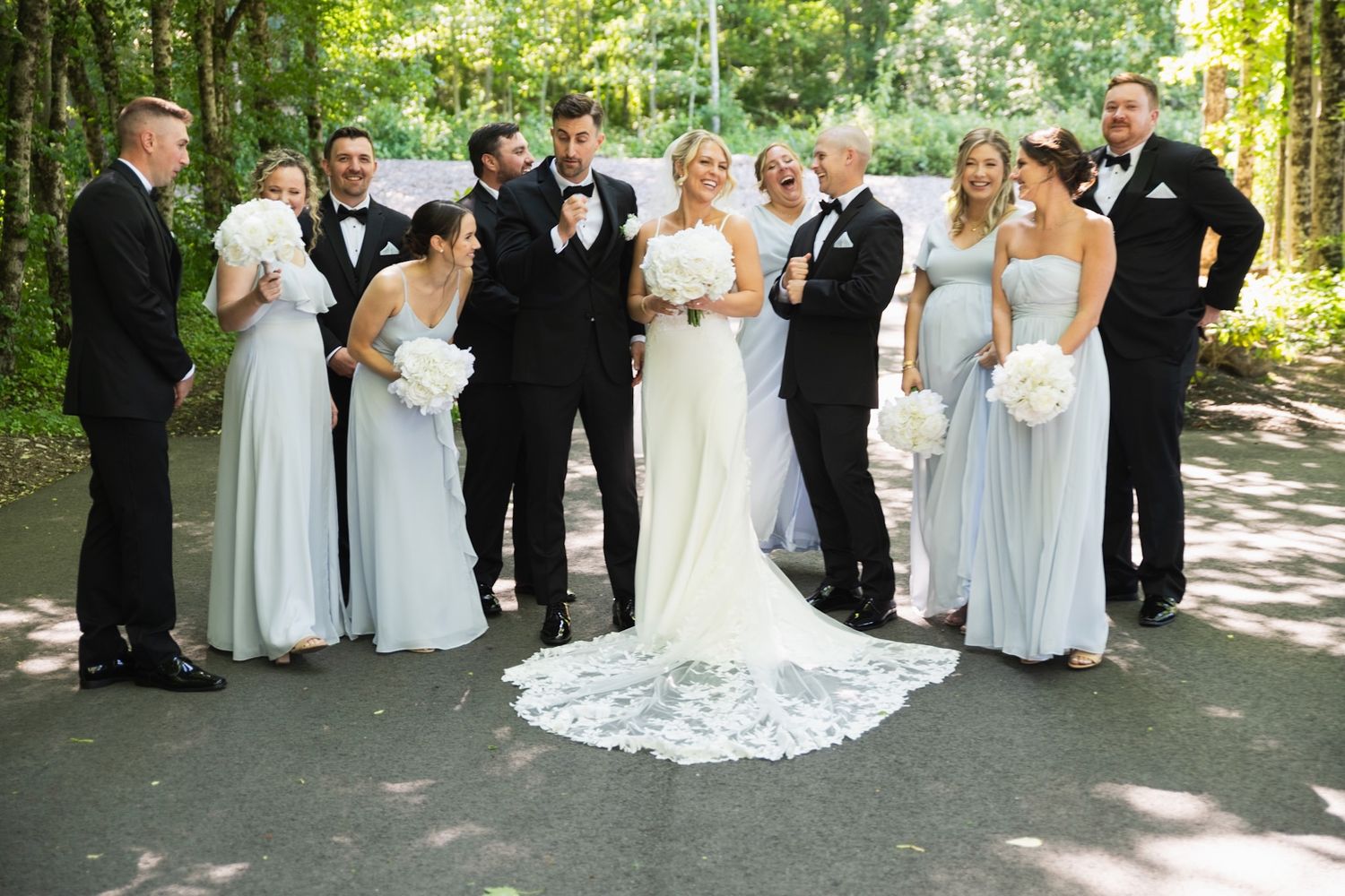 Wedding party poses outdoors in formal attire with bridesmaids in light dresses and groomsmen in black suits.