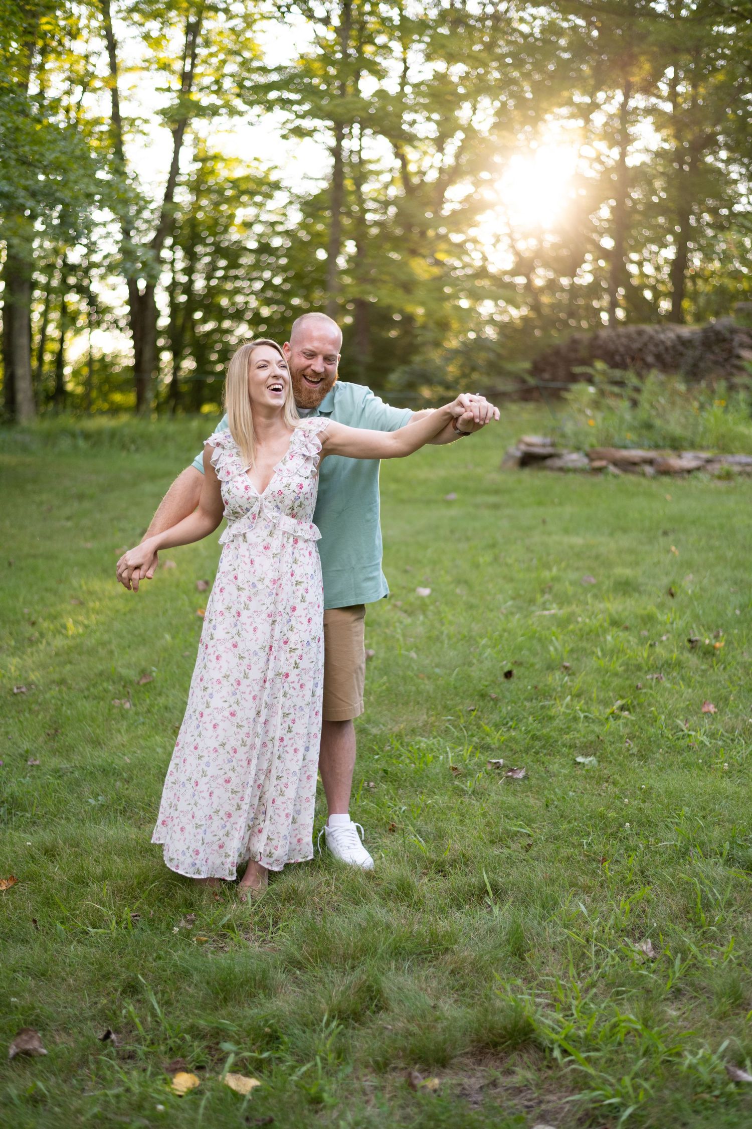A joyful couple dances together on a grassy hill during golden hour sunset.