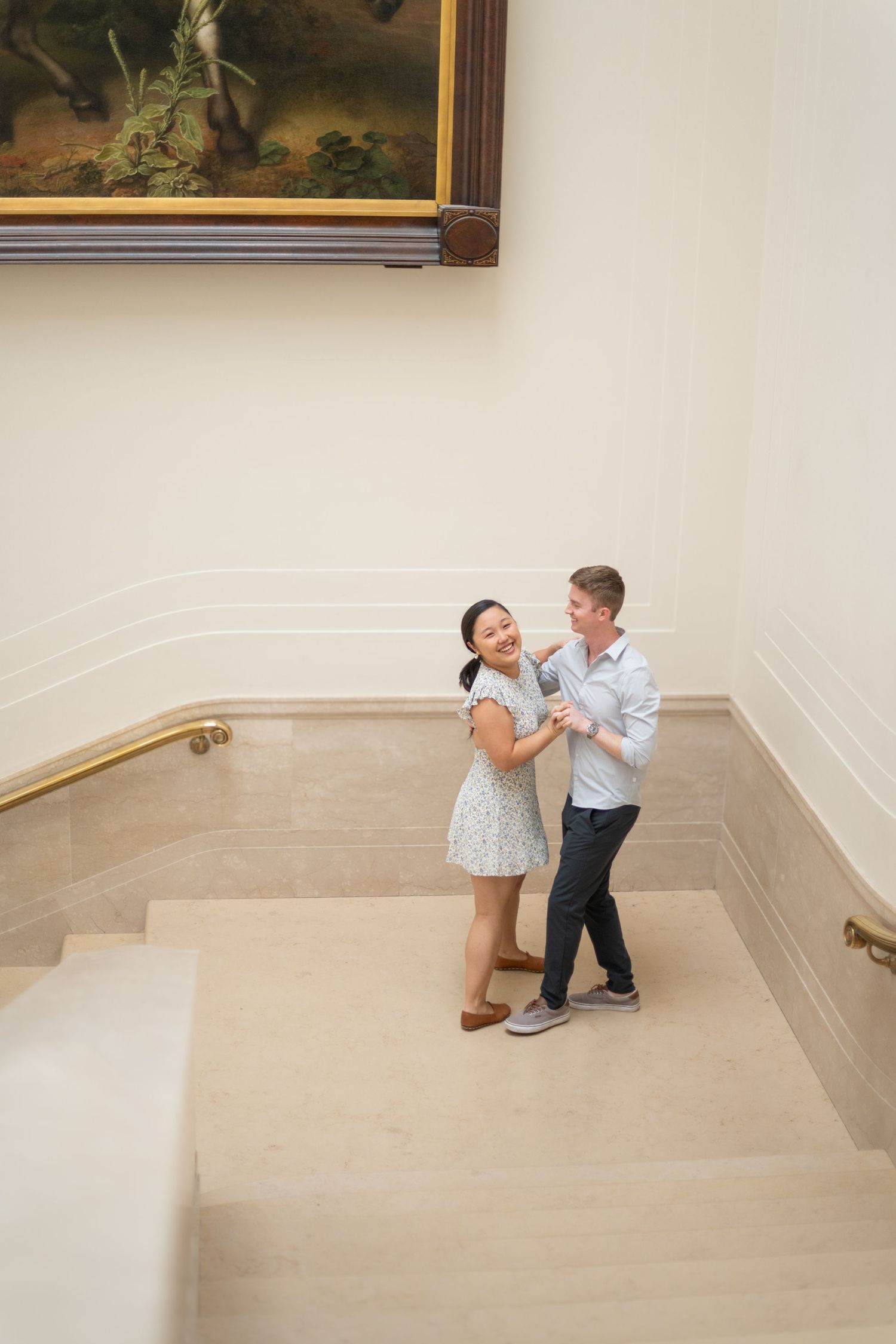 An indoor proposal series showing a surprise moment on marble steps with artwork in the background.