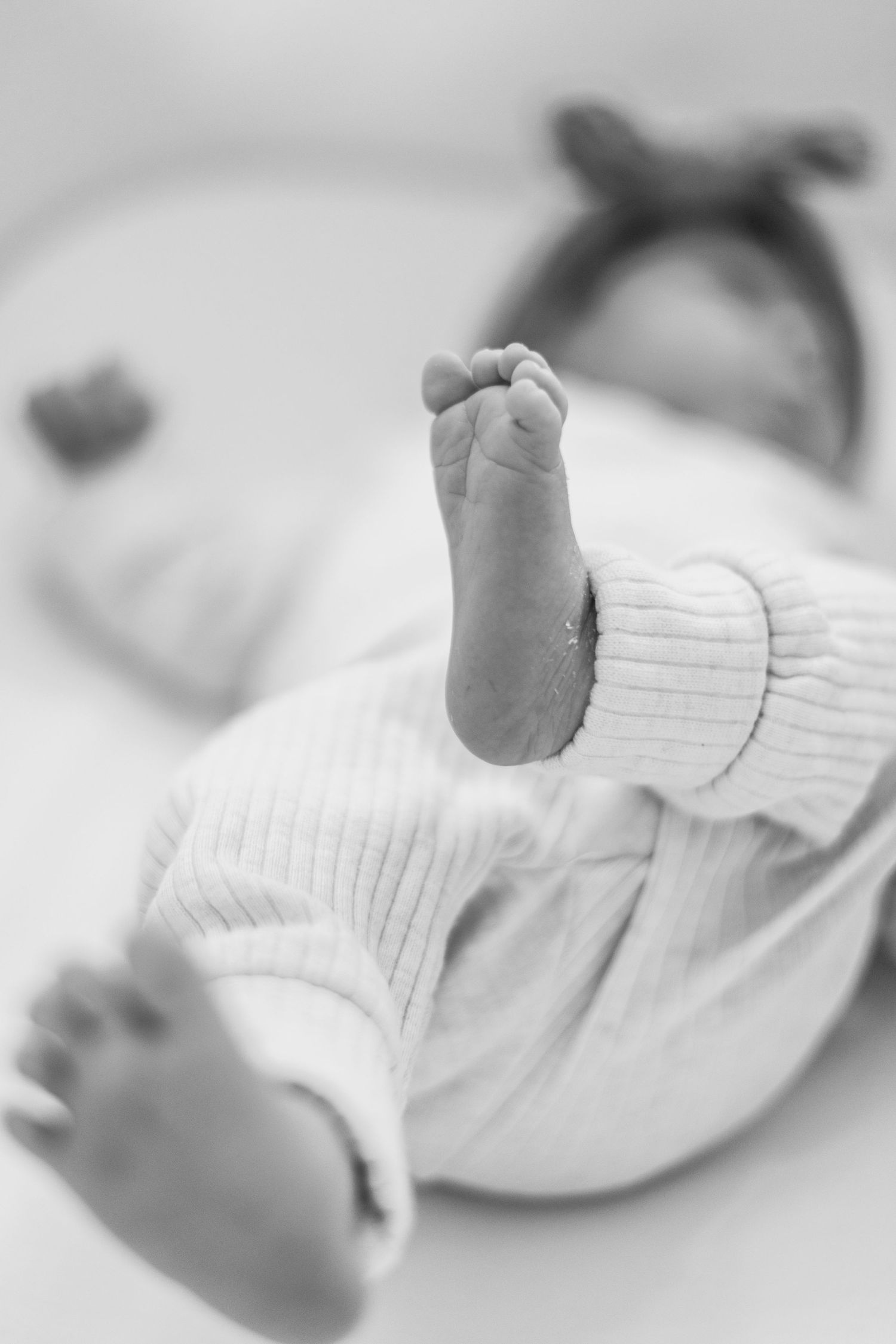 Close-up black and white photos show tiny newborn baby feet in soft white fabric.