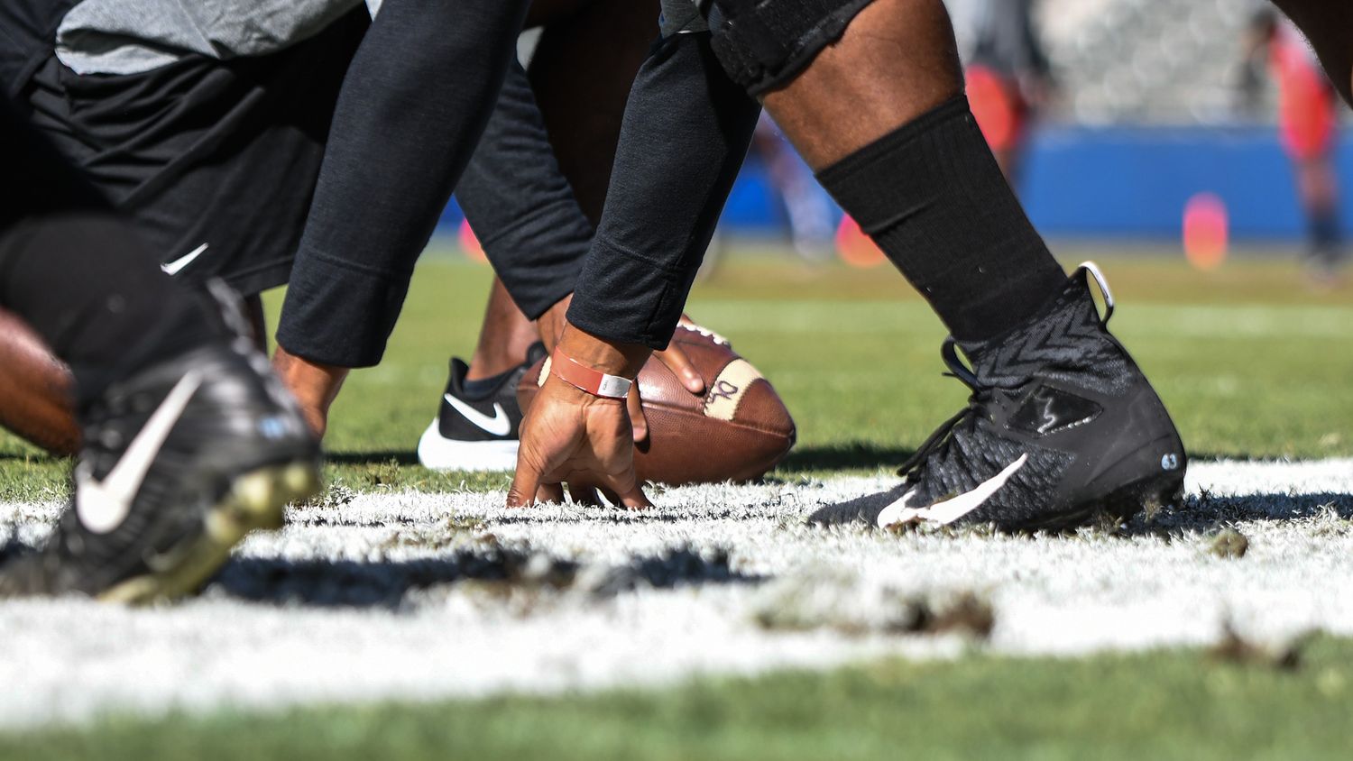 Close-up of NFL players at the line of scrimmage, center snapping football in Nike cleats on grass field.